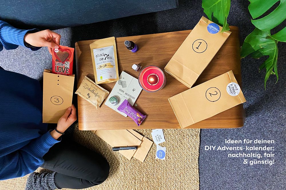 Person gestaltet DIY-Adventskalender mit nachhaltigen Produkten wie Schokolade und Kerze auf einem Tisch.