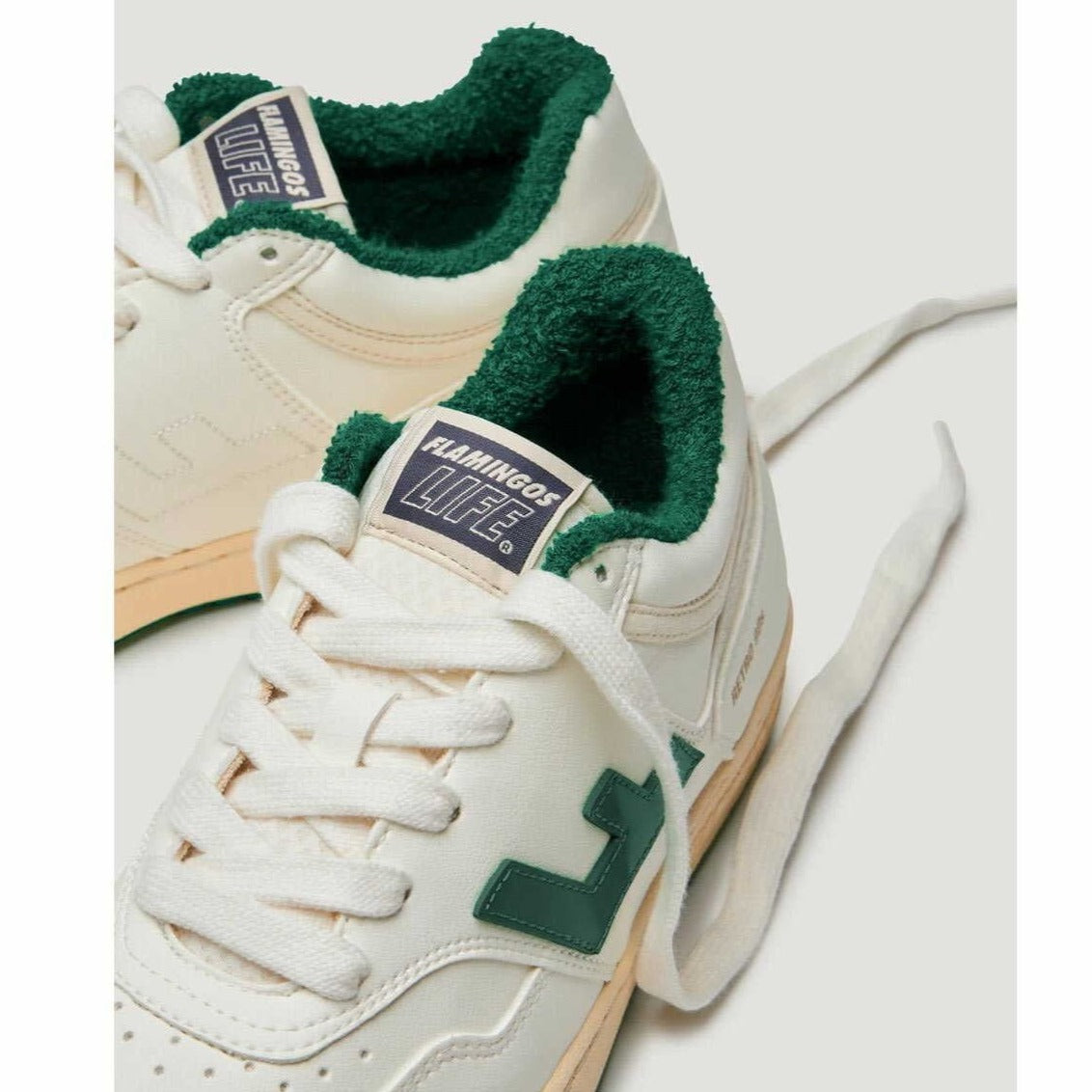 Weiße Turnschuhe mit grünem Plüschfutter und grünem Logo auf der Seite, auf der Zunge steht "FLAMINGOS LIFE".