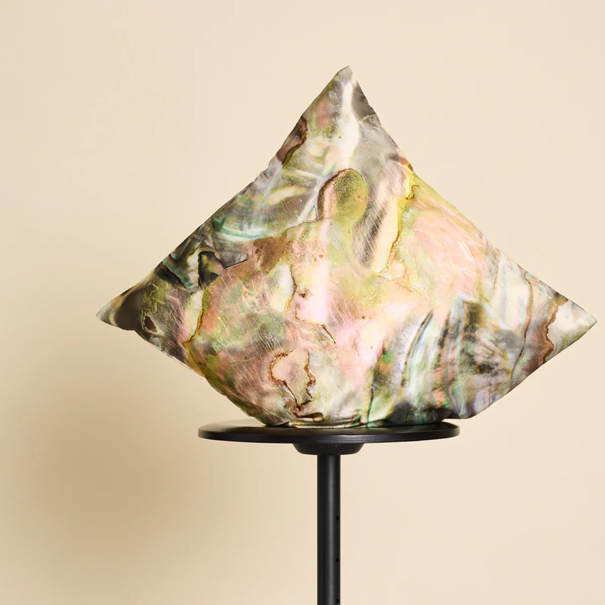 Abstrakte Skulptur auf einem schwarzen Ständer vor einem beigefarbenen Hintergrund.