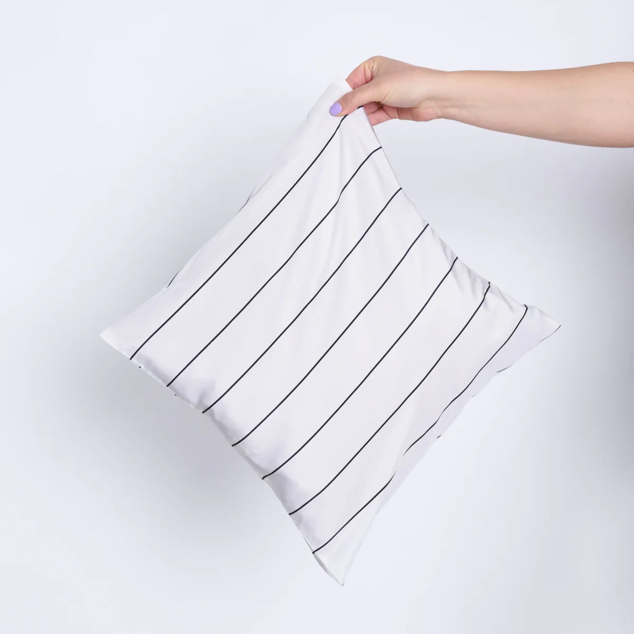 Eine Hand hält ein weißes Kissen mit schwarzen Streifen vor einem hellgrauen Hintergrund.