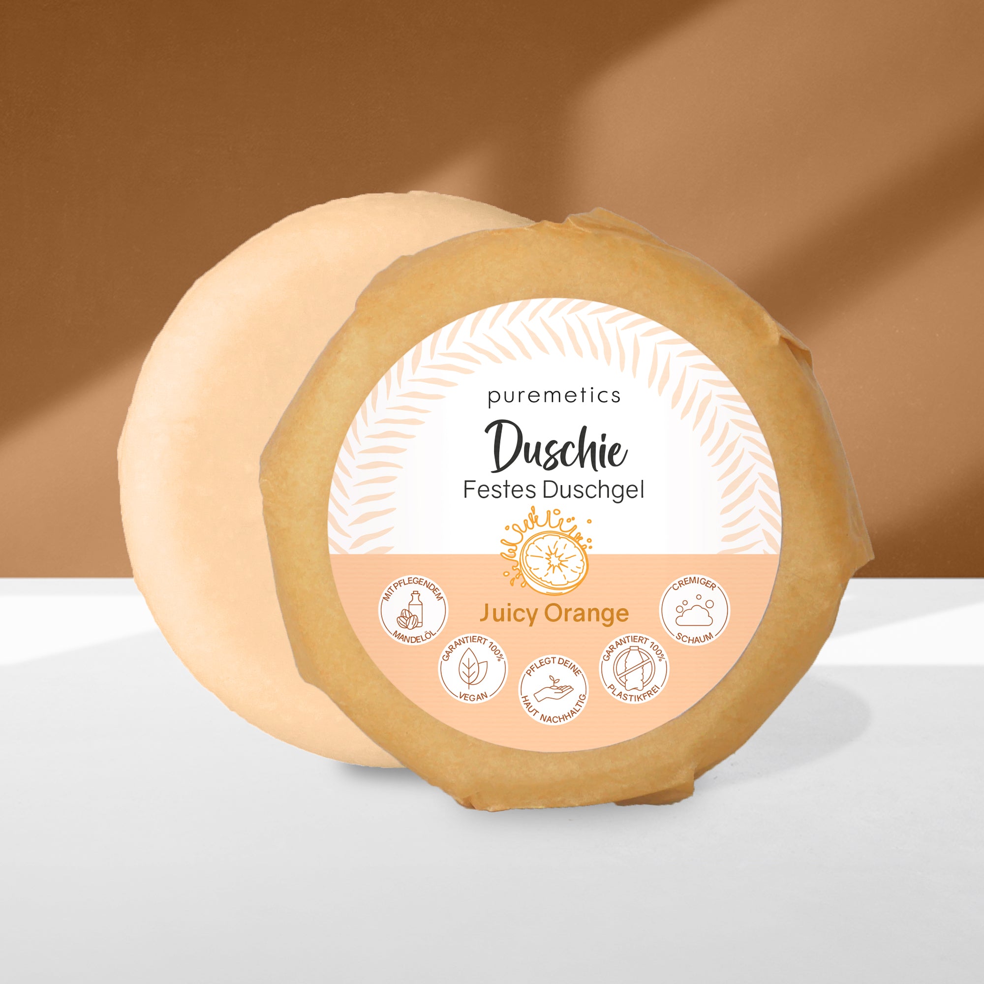 Rundes festes Duschgel "Dusche" von puremetics mit orangenem Etikett und Symbolen, auf hellem Hintergrund.