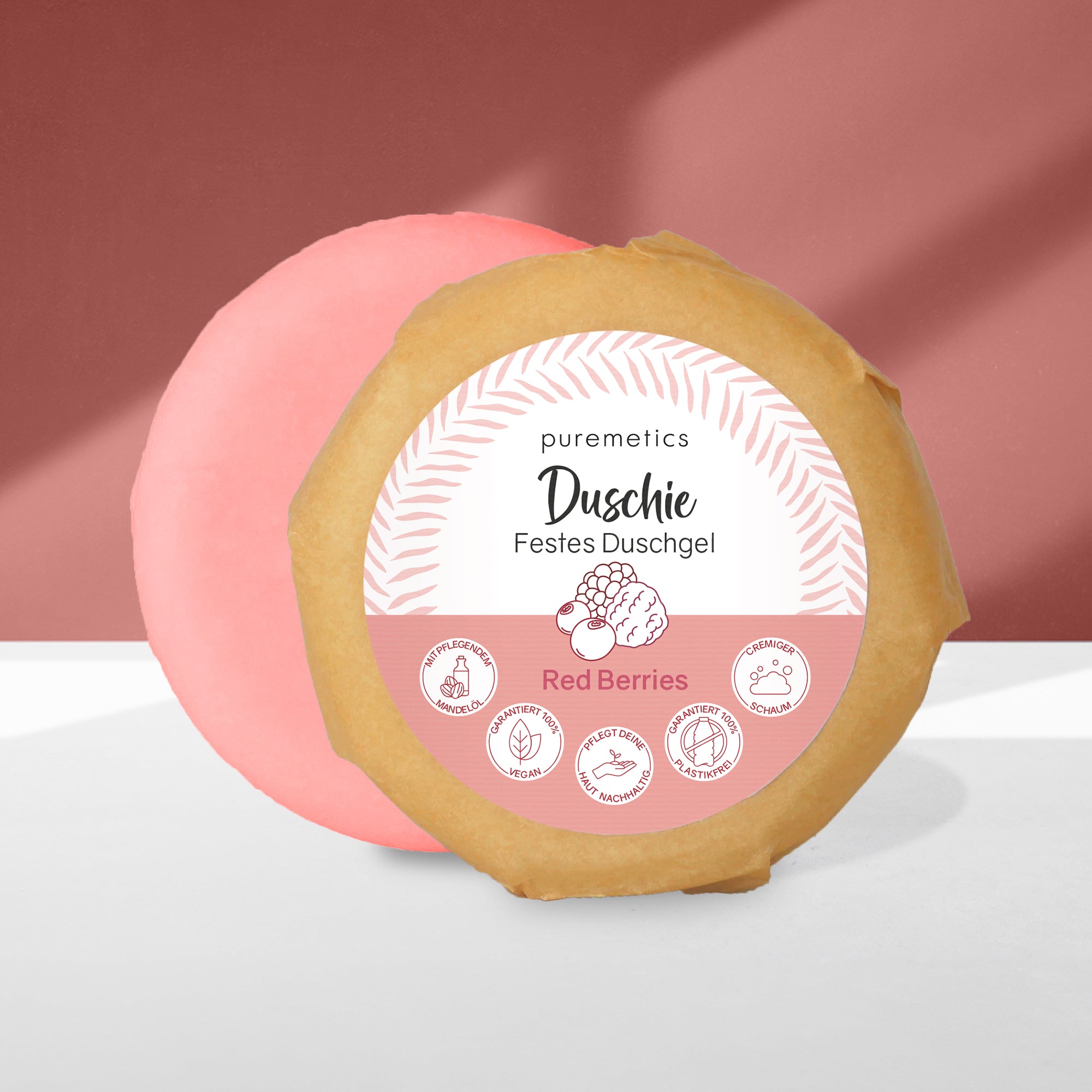 Zwei runde Seifenstücke mit Etikett "Duschie Festes Duschgel Red Berries" vor einem rot-weißen Hintergrund.