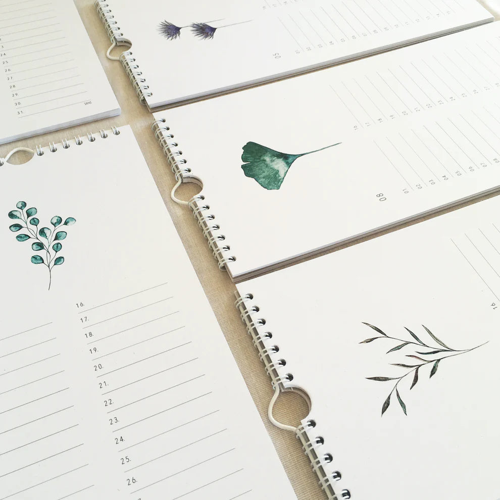 Mehrere spiralgebundene Wandkalender mit minimalistischen botanischen Illustrationen und linierten Feldern für Termine sind auf einer hellen Oberfläche ausgelegt. Jeder Kalender zeigt ein anderes Pflanzen- oder Blattmotiv.
