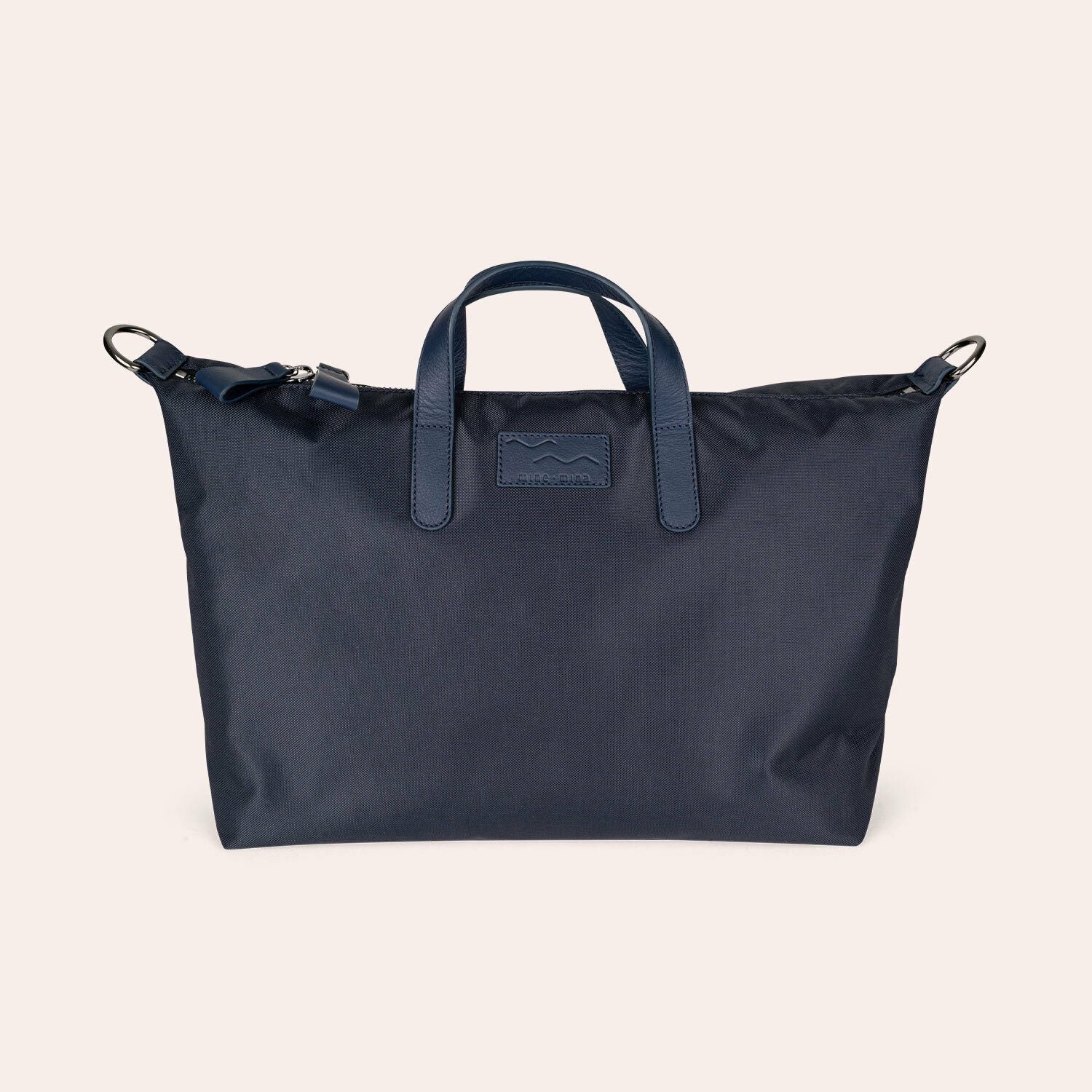 Eine marineblaue Tragetasche mit kurzen Henkeln, einem Reißverschluss und abnehmbaren Schulterriemenhaken, die vor einem hellbeigen Hintergrund präsentiert wird.