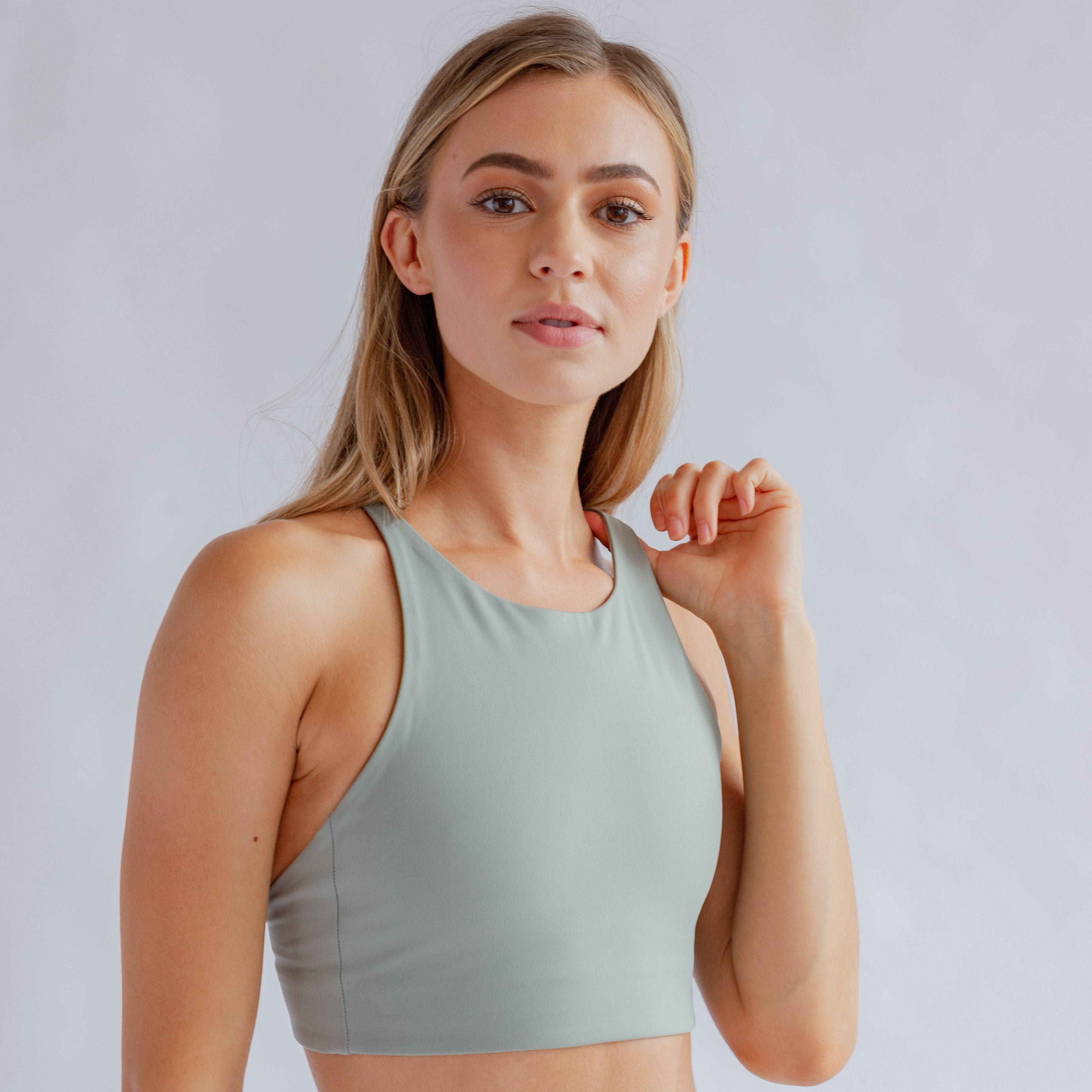 Frau in einem grauen Sportoberteil vor grauem Hintergrund, mit leicht geneigtem Kopf und leichtem Lächeln.