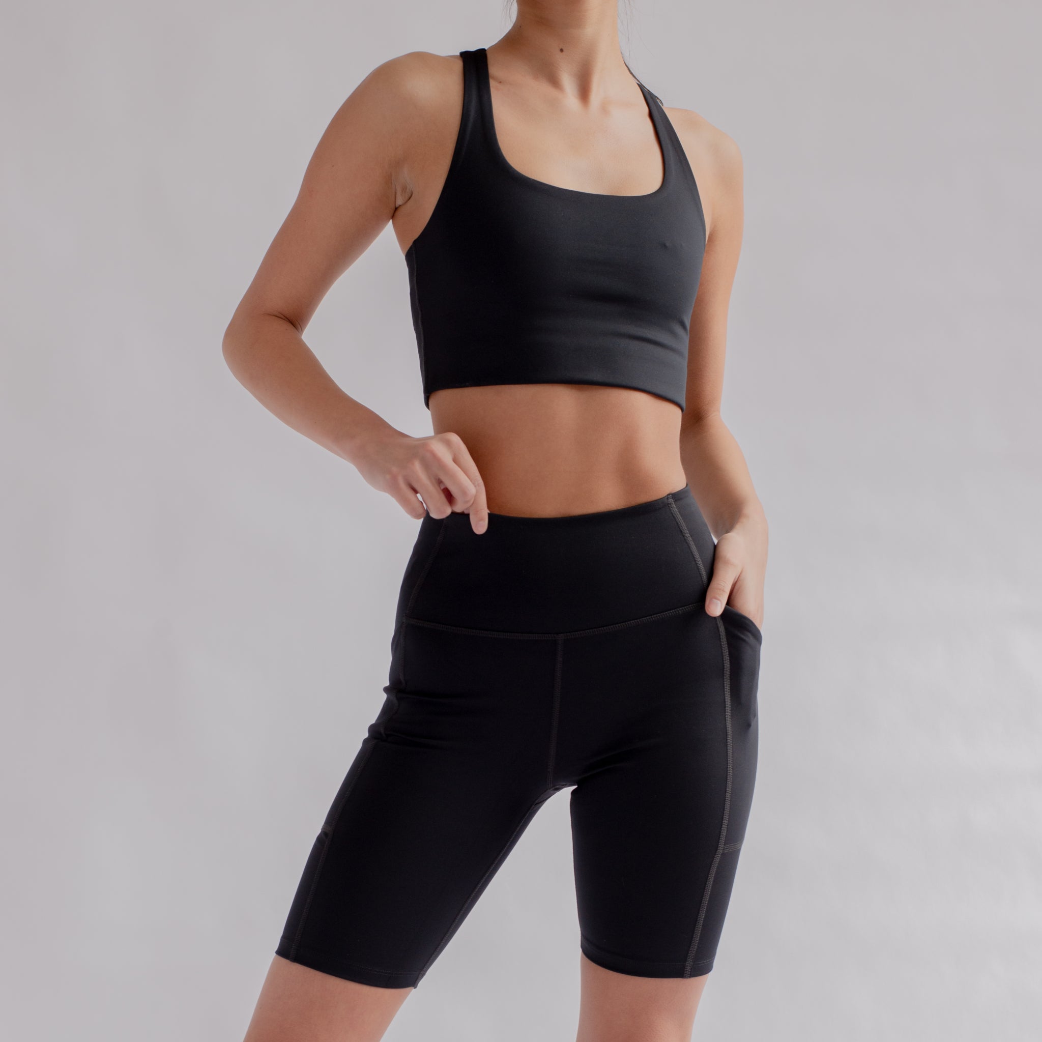 Eine Person trägt ein schwarzes Sportoberteil und Shorts vor neutralem Hintergrund.