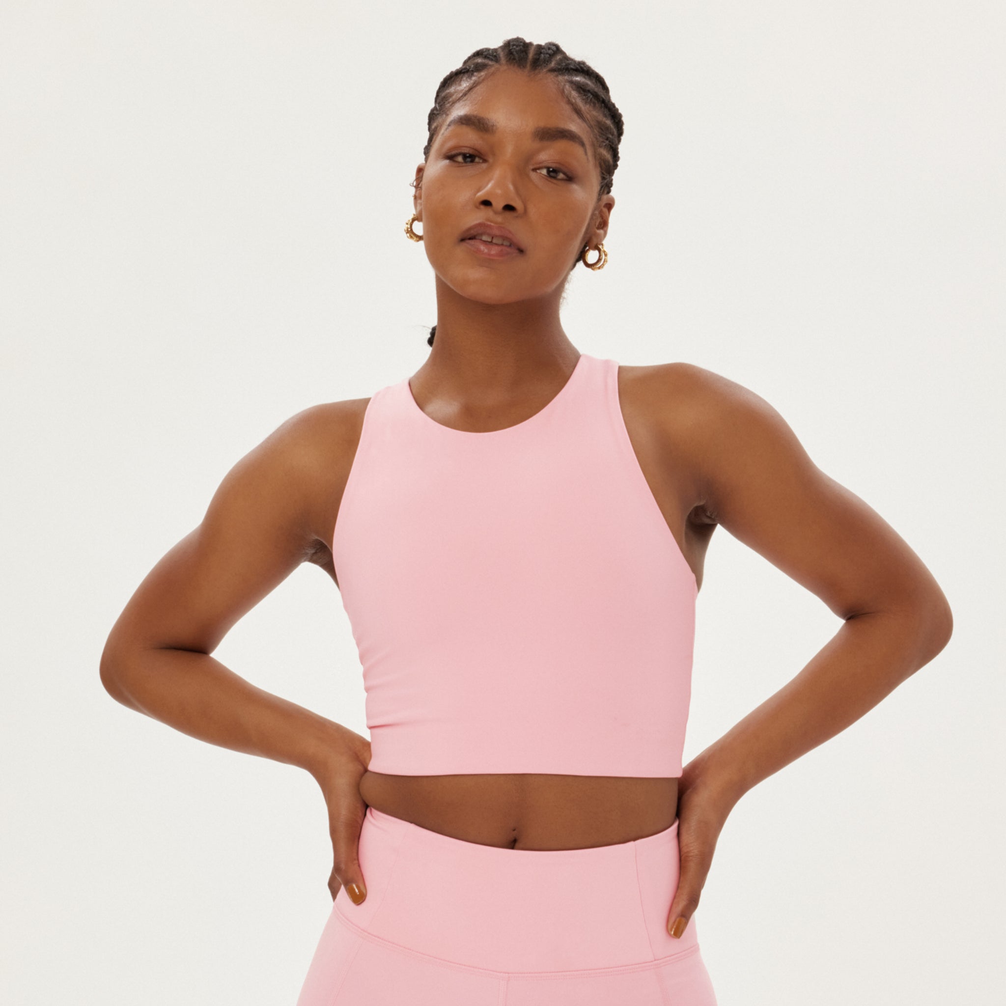 Eine Frau in rosa Sportbekleidung mit verschränkten Armen vor einem neutralen Hintergrund.
