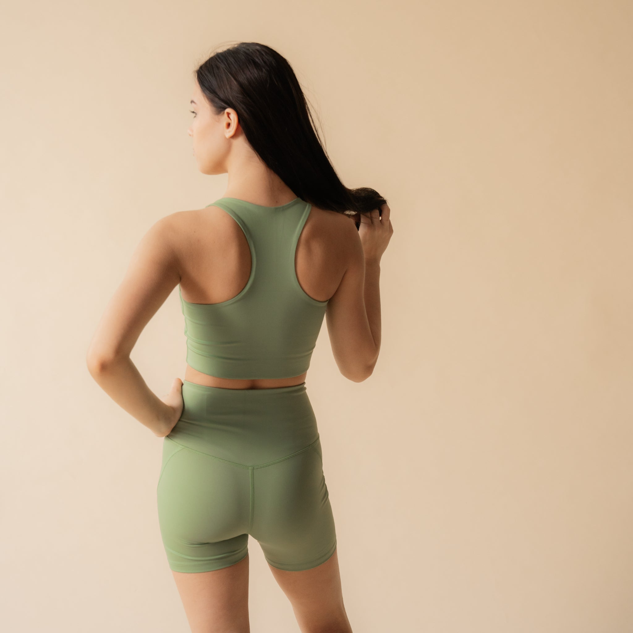 Frau in grüner Sportkleidung von hinten vor einem beigen Hintergrund.