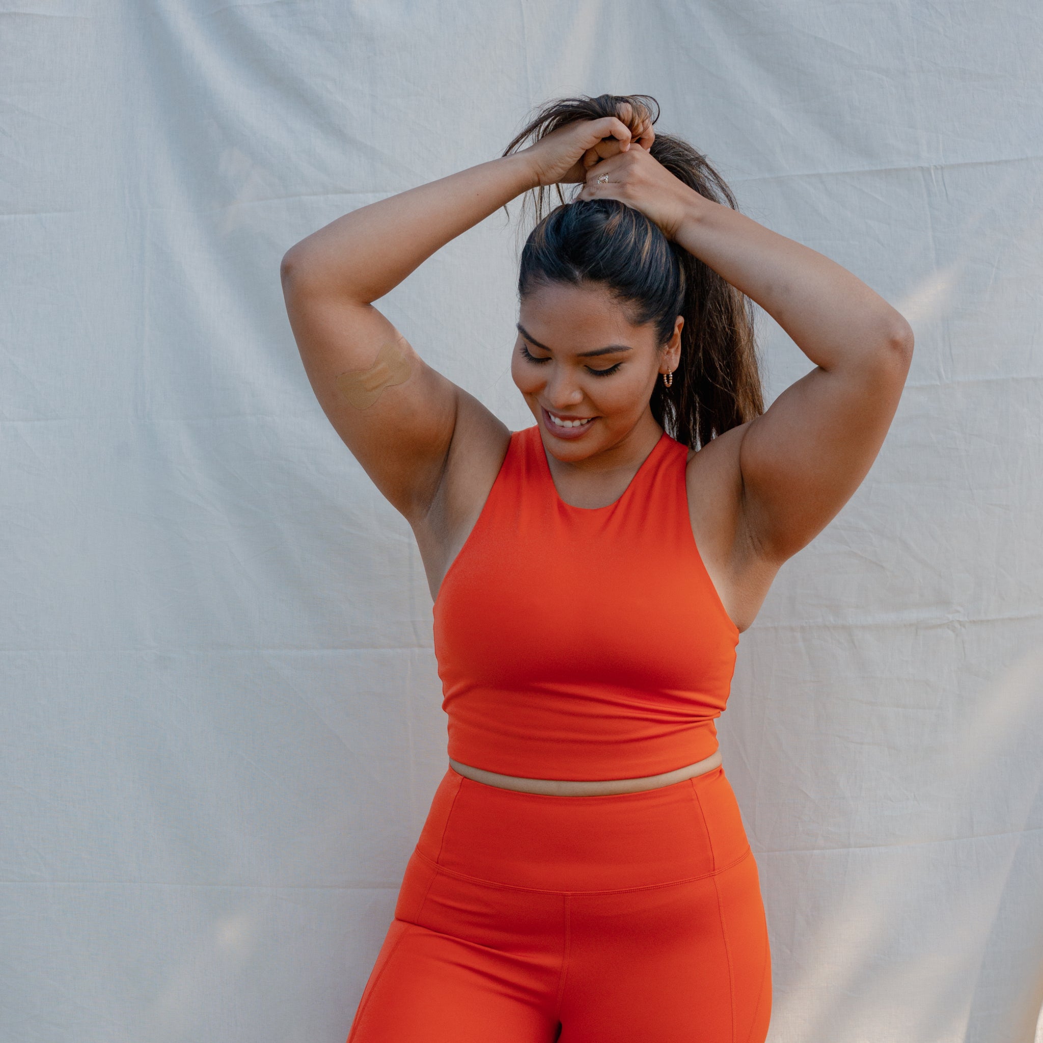 Frau in rotem Sportoutfit steht vor einem weißen Hintergrund und bindet ihre Haare.