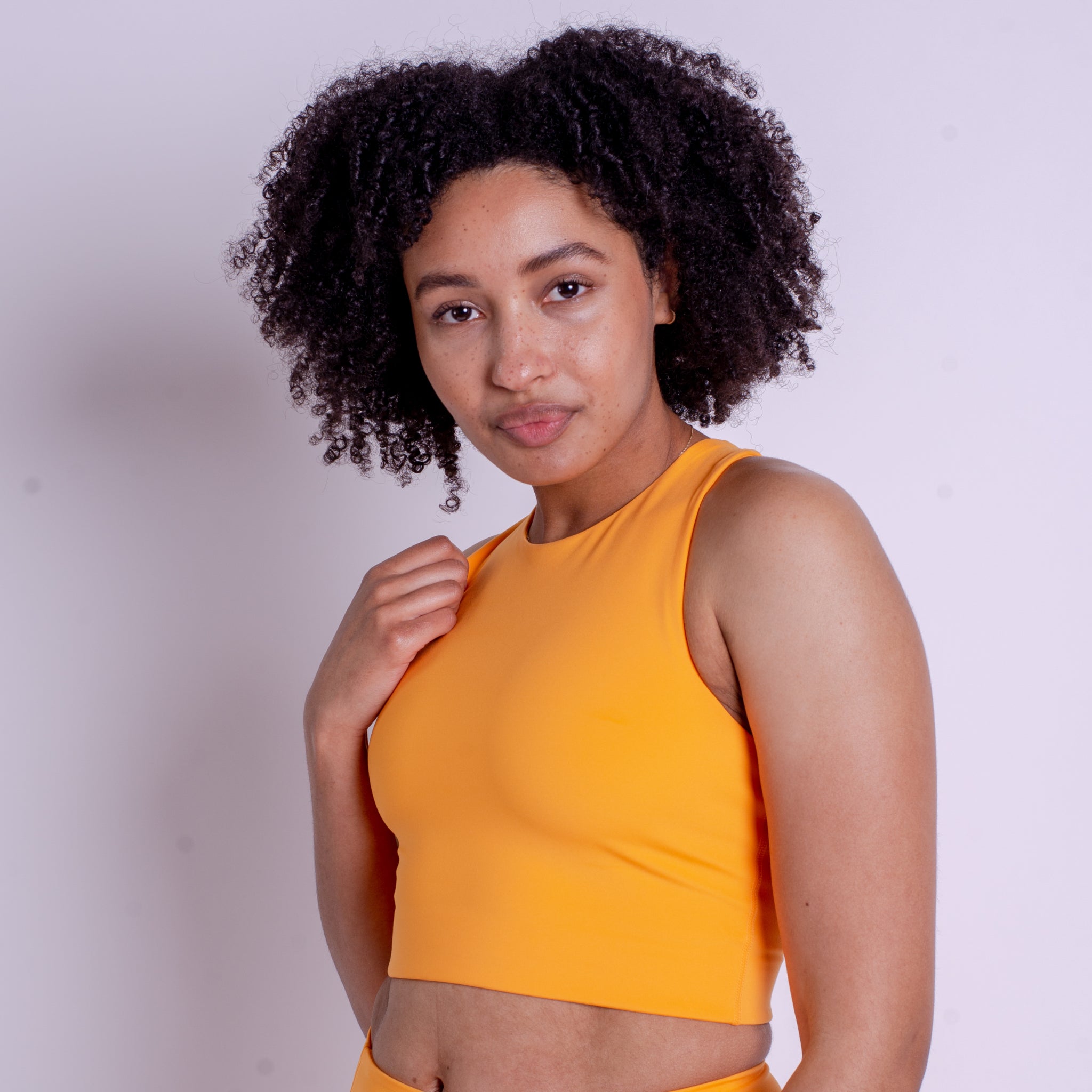Frau mit lockigem Haar trägt ein gelbes Oberteil und blickt in die Kamera.