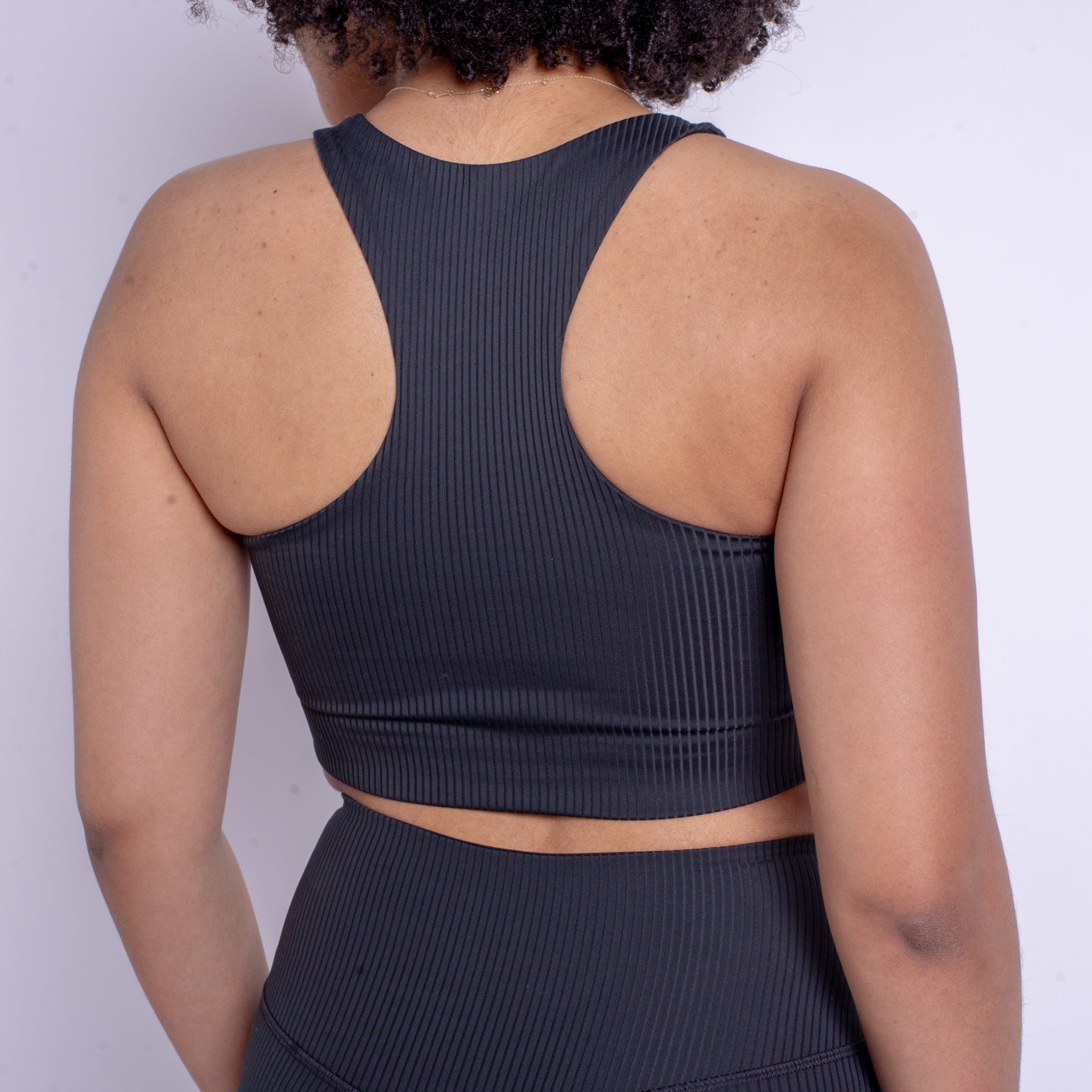 Person in einem gerippten, ärmellosen schwarzen Top und Leggings, von hinten fotografiert.