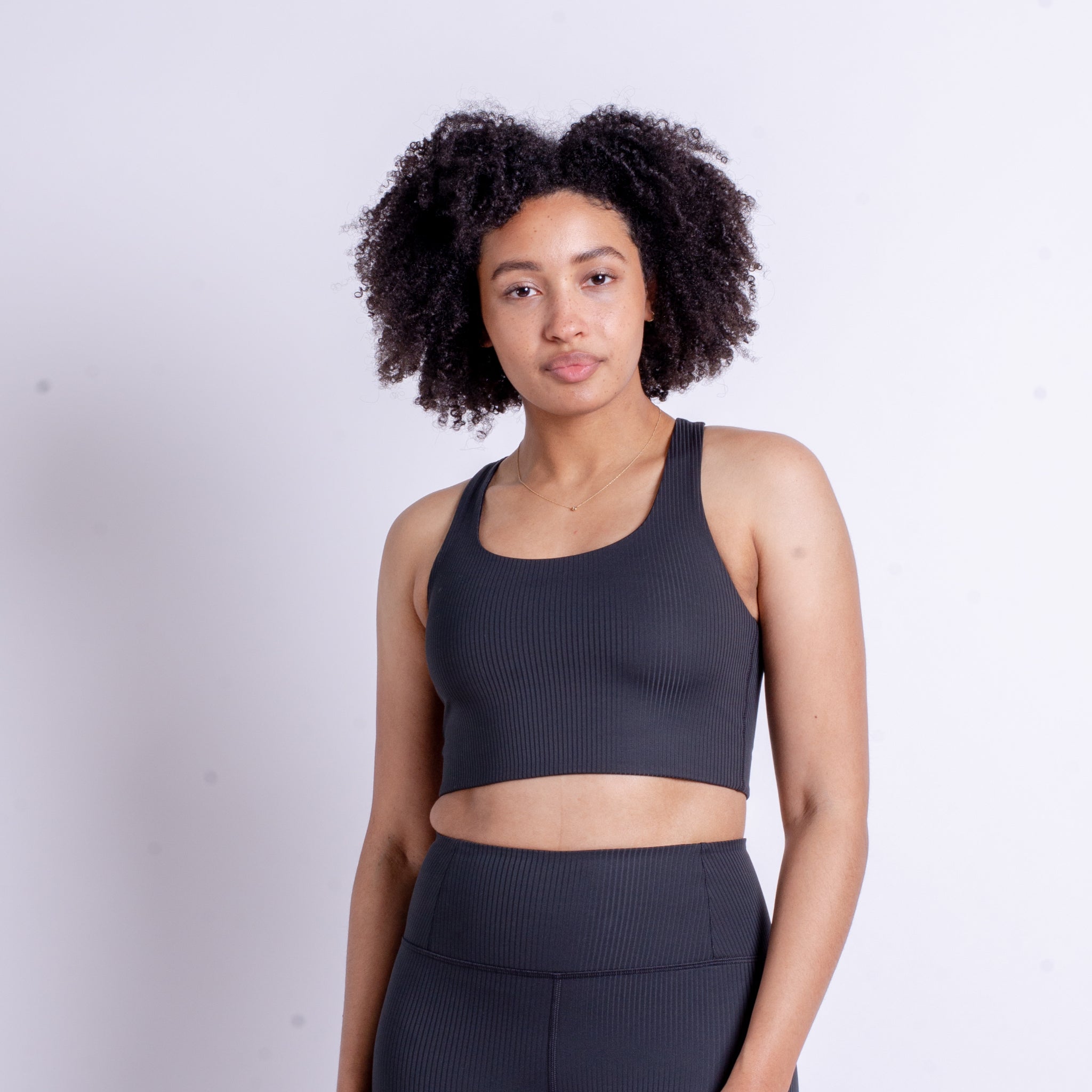 Eine Frau in schwarzer Sportkleidung steht vor einem weißen Hintergrund.