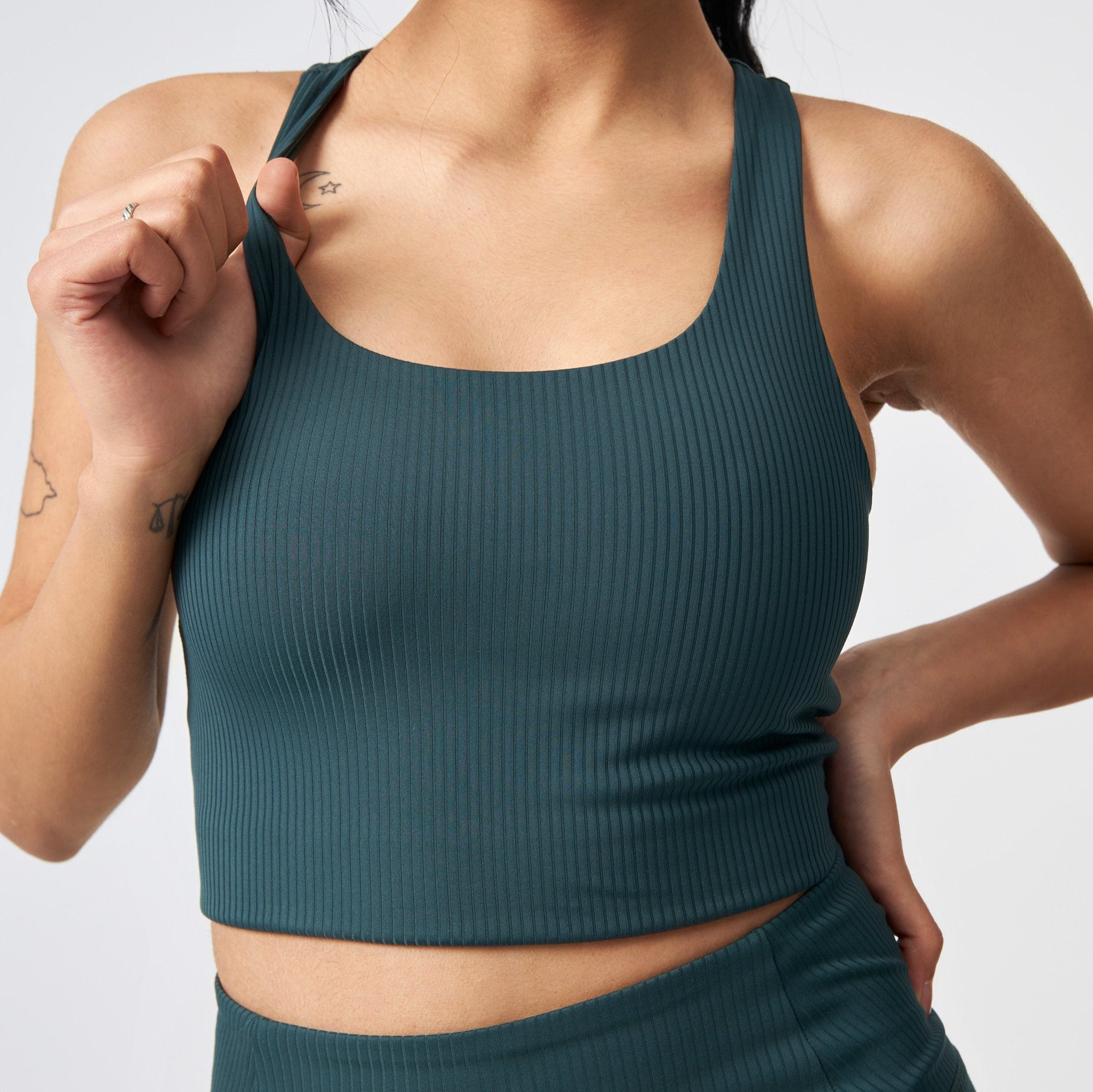 Frau in einem gerippten, grünen Sport-Top mit Tattoos auf dem Arm.