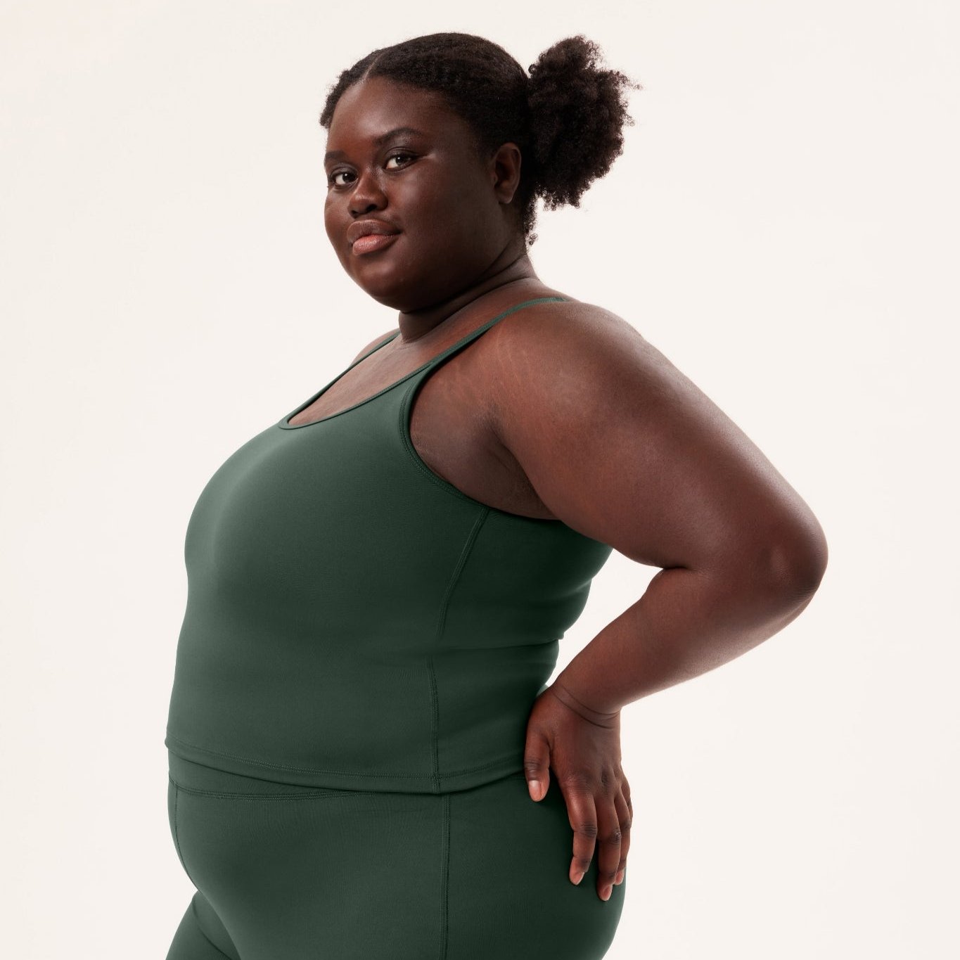 Eine Person in grüner Sportkleidung blickt selbstbewusst zur Seite vor einem neutralen Hintergrund.