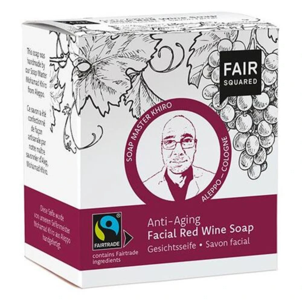 Eine Schachtel der FAIR SQUARED Anti-Aging Gesichtsseife mit Rotwein enthält Abbildungen von Weintrauben, ein Porträt des Seifenmeisters Khiro und eine Fairtrade-Zertifizierung. Der Text ist auf Englisch, Deutsch und Französisch.