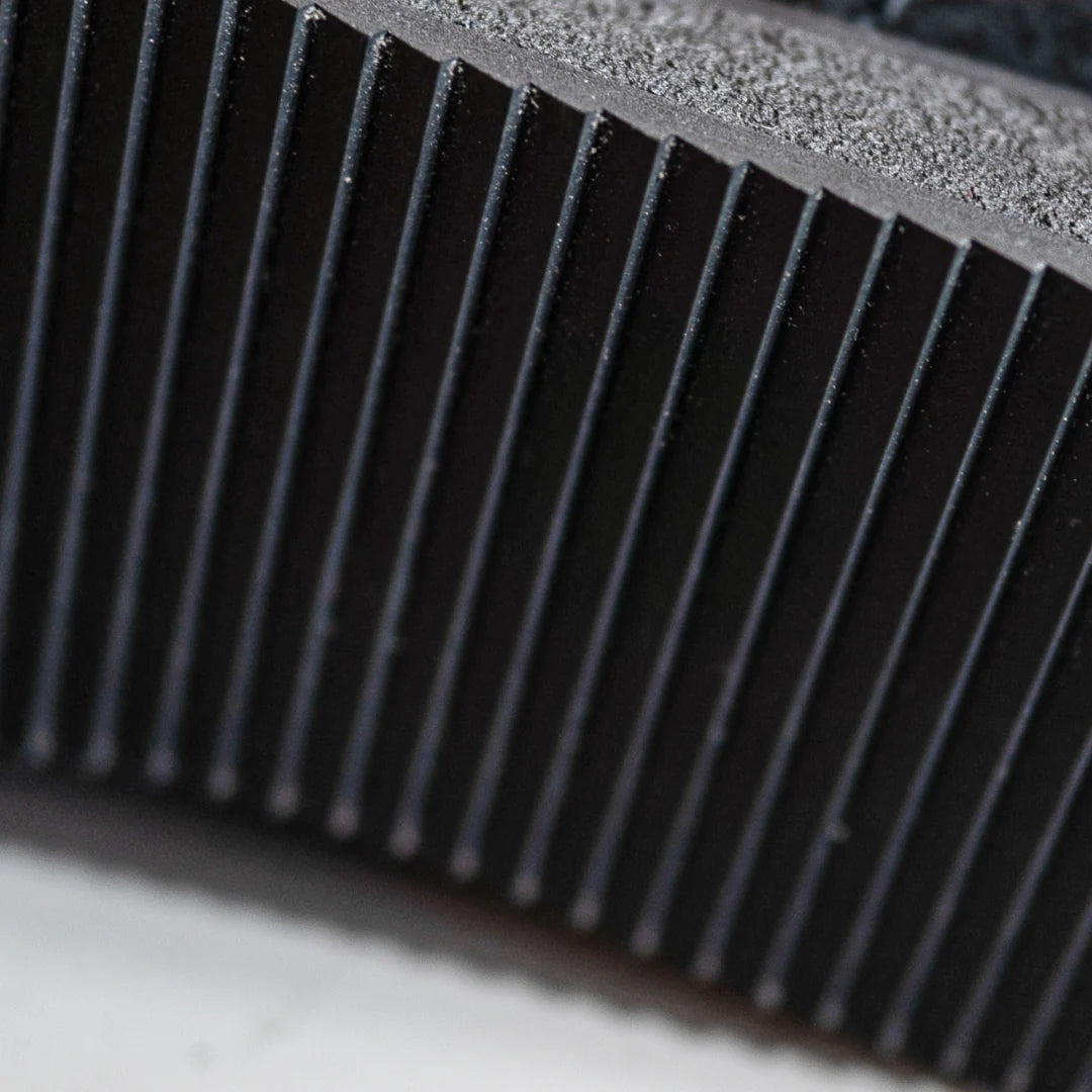 Nahaufnahme einer schwarzen Schuhsohle mit vertikalen Rillen, die das strukturierte Gummimaterial und die feinen Details des Laufflächenprofils zeigen.