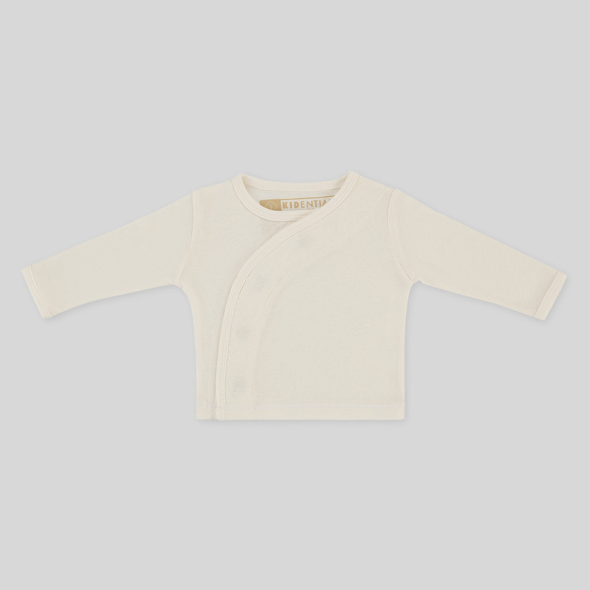 Beigefarbenes Baby-Langarmshirt mit seitlicher Knopfleiste auf grauem Hintergrund.