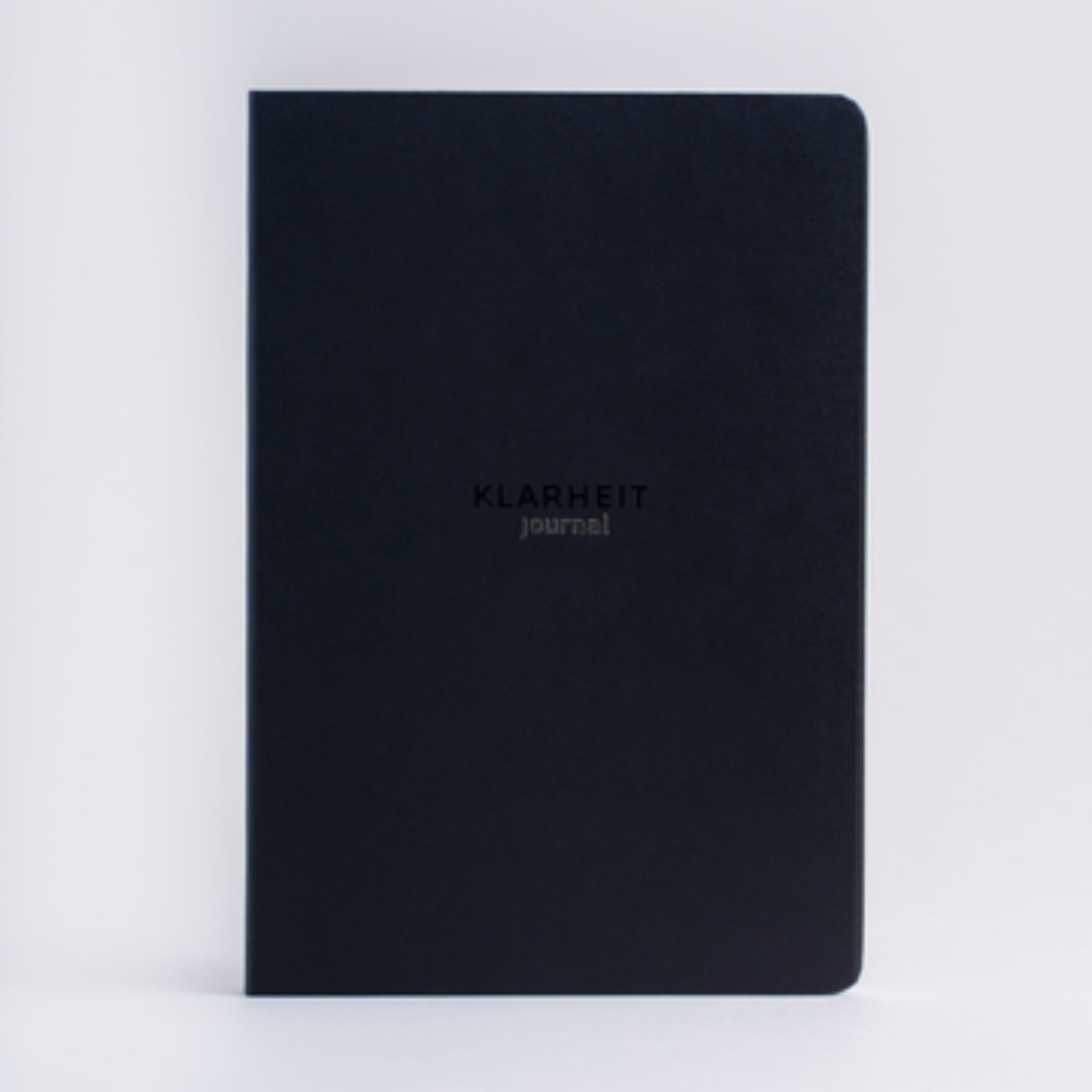 Schwarzes Notizbuch mit der Aufschrift „KLARHEIT journal“ auf dem Einband, vor weißem Hintergrund.