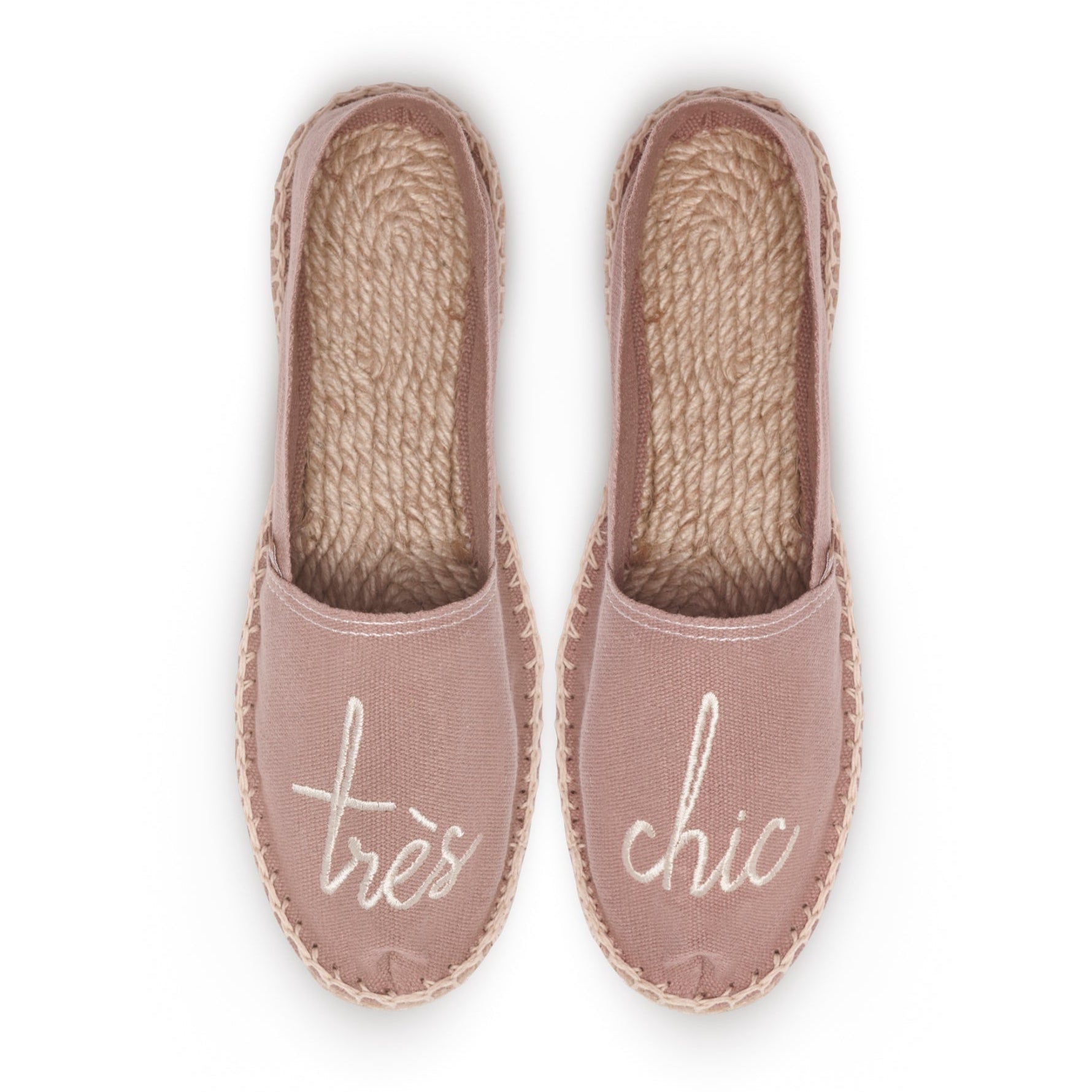Rosa Espadrilles von oben, mit den Worten "très" und "chic" auf den Schuhen in hellen Buchstaben bestickt.