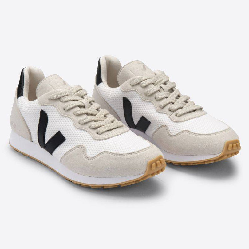 Ein Paar weiße und beigefarbene Turnschuhe mit schwarzem V-Logo an den Seiten, weißen Schnürsenkeln und hellbraunen Gummisohlen auf einem einfarbigen hellgrauen Hintergrund.