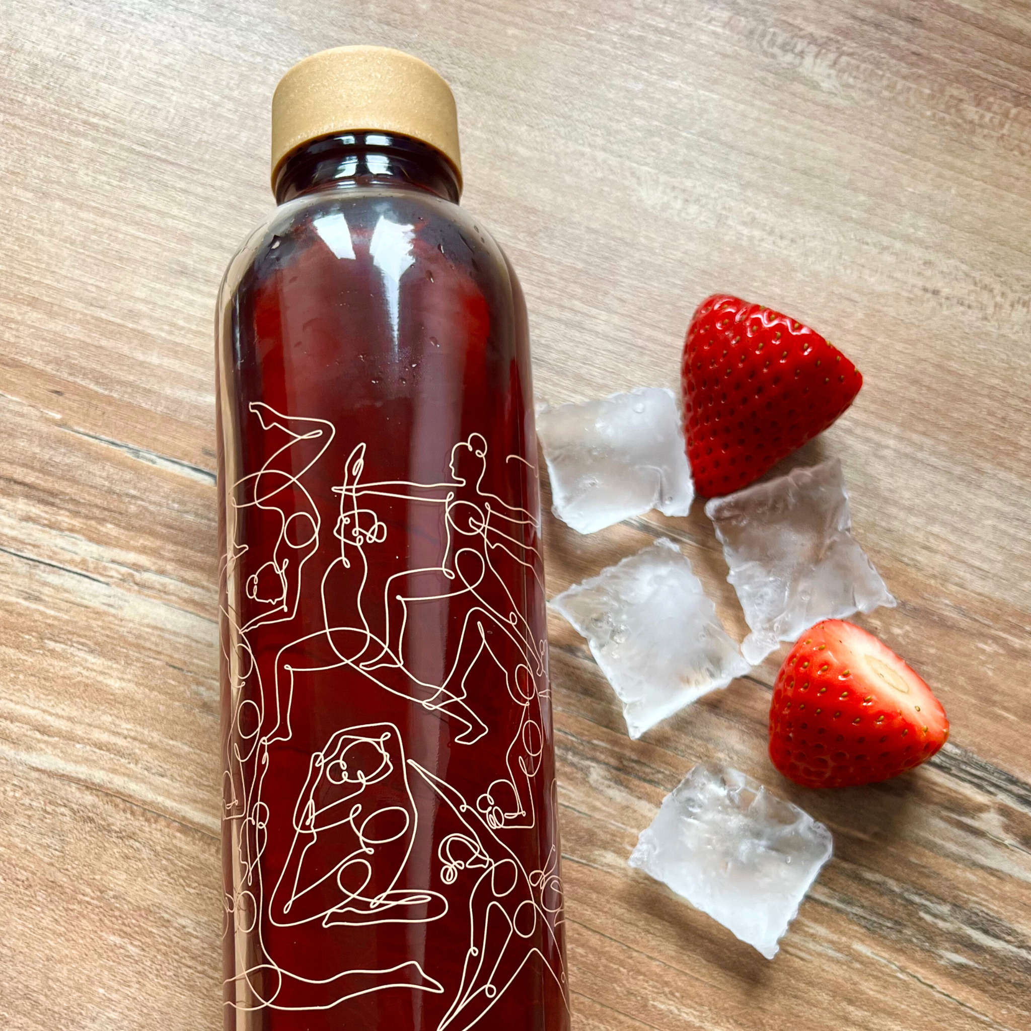 Eine Flasche mit rotem Getränk, verziert mit Zeichnungen, liegt neben Eiswürfeln und halbierten Erdbeeren auf Holz.