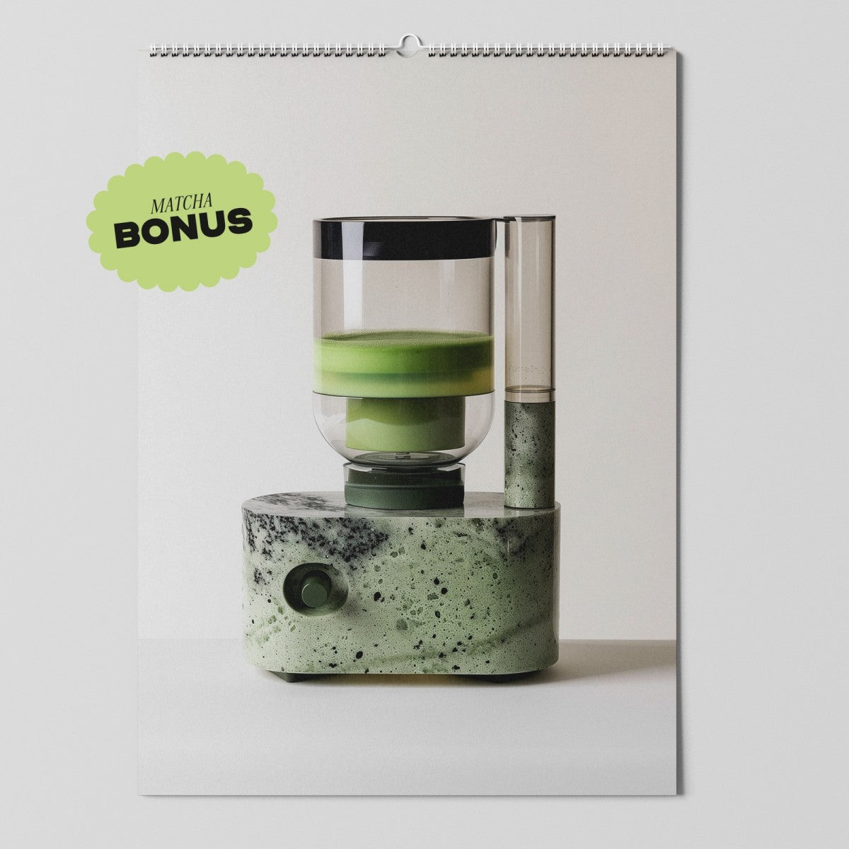 Ein moderner Matcha-Teezubereiter mit grün gesprenkeltem Sockel und durchsichtigen Behältern, ausgestellt auf einem Wandkalender. Oben links befindet sich ein grünes Abzeichen mit der Aufschrift MATCHA BONUS.