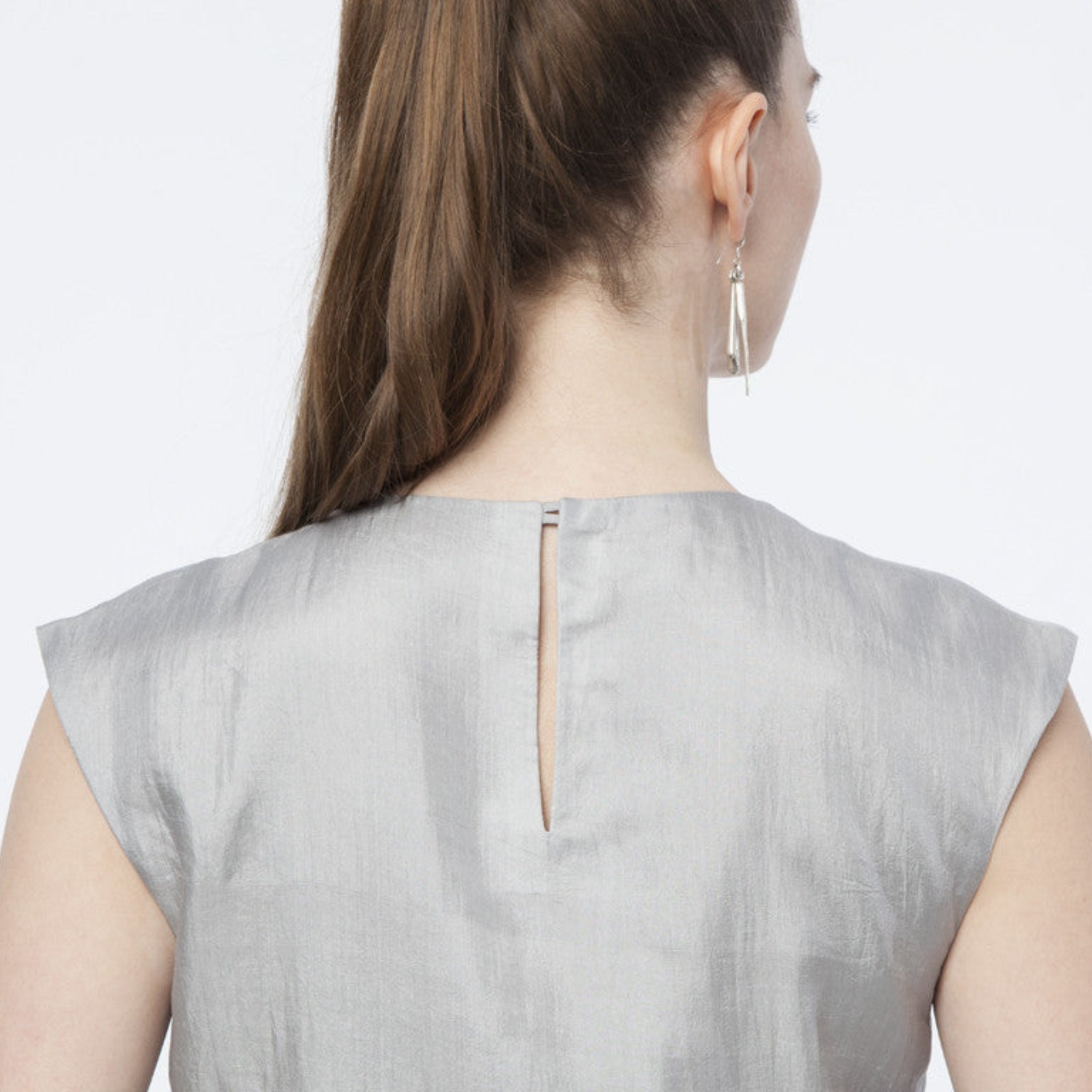 Rückansicht einer Frau mit langem Haar, die ein graues Kleid mit Rückenschlitz und silbernen Ohrringen trägt.