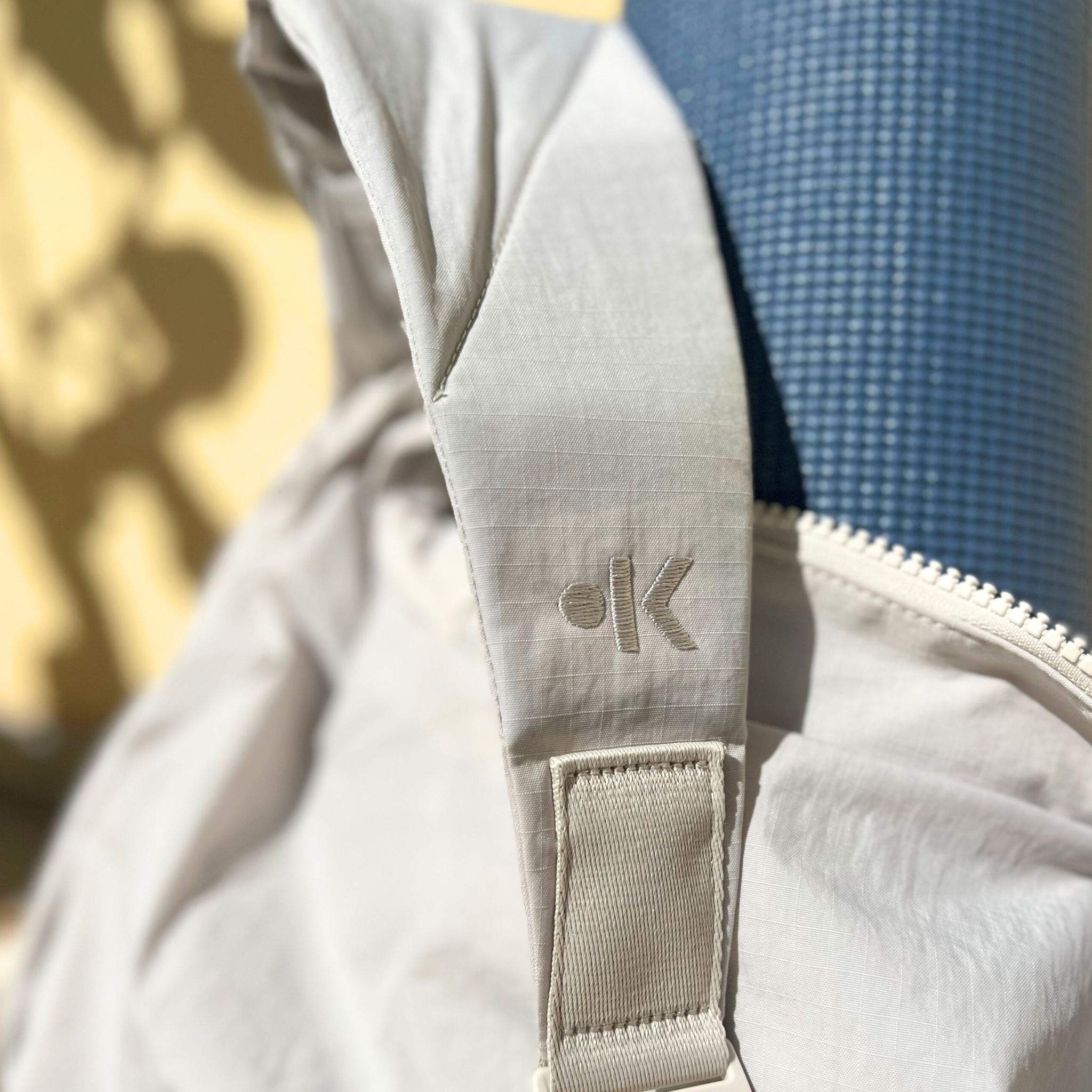 Nahaufnahme eines beigen Riemens mit gesticktem Logo, der neben eine blaue Matte gelegt ist.