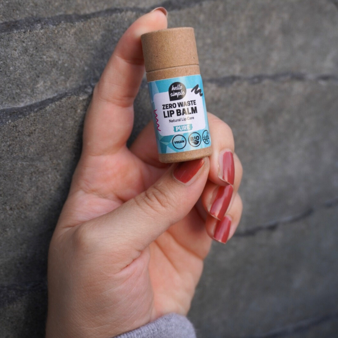 Hand hält eine plastikfreie Lip Balm-Verpackung vor einer grauen Wand.