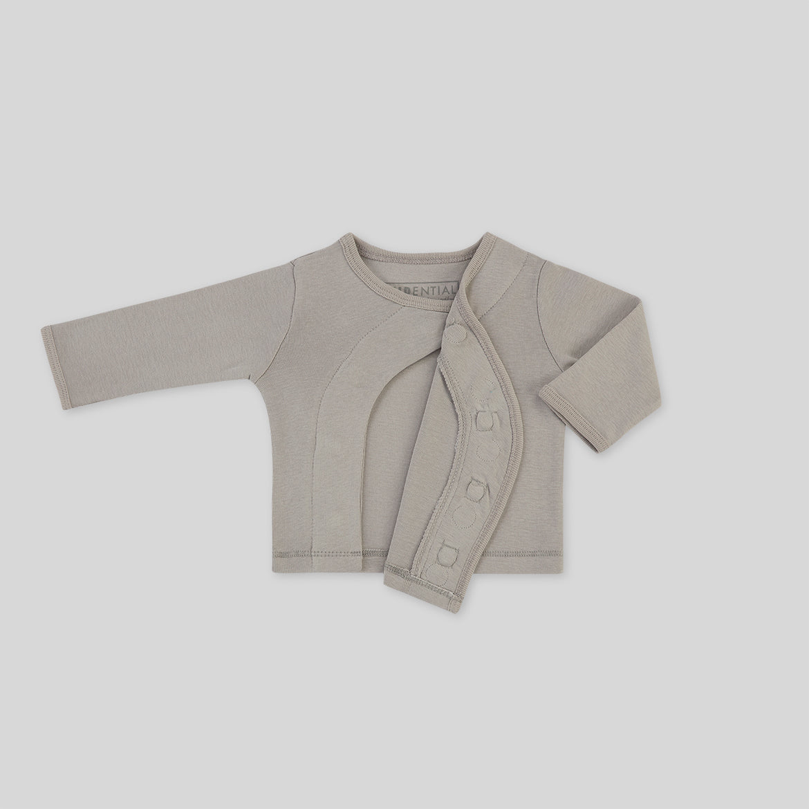 Graue Babyjacke mit langen Ärmeln und seitlich zu öffnendem Verschluss, auf grauem Hintergrund.