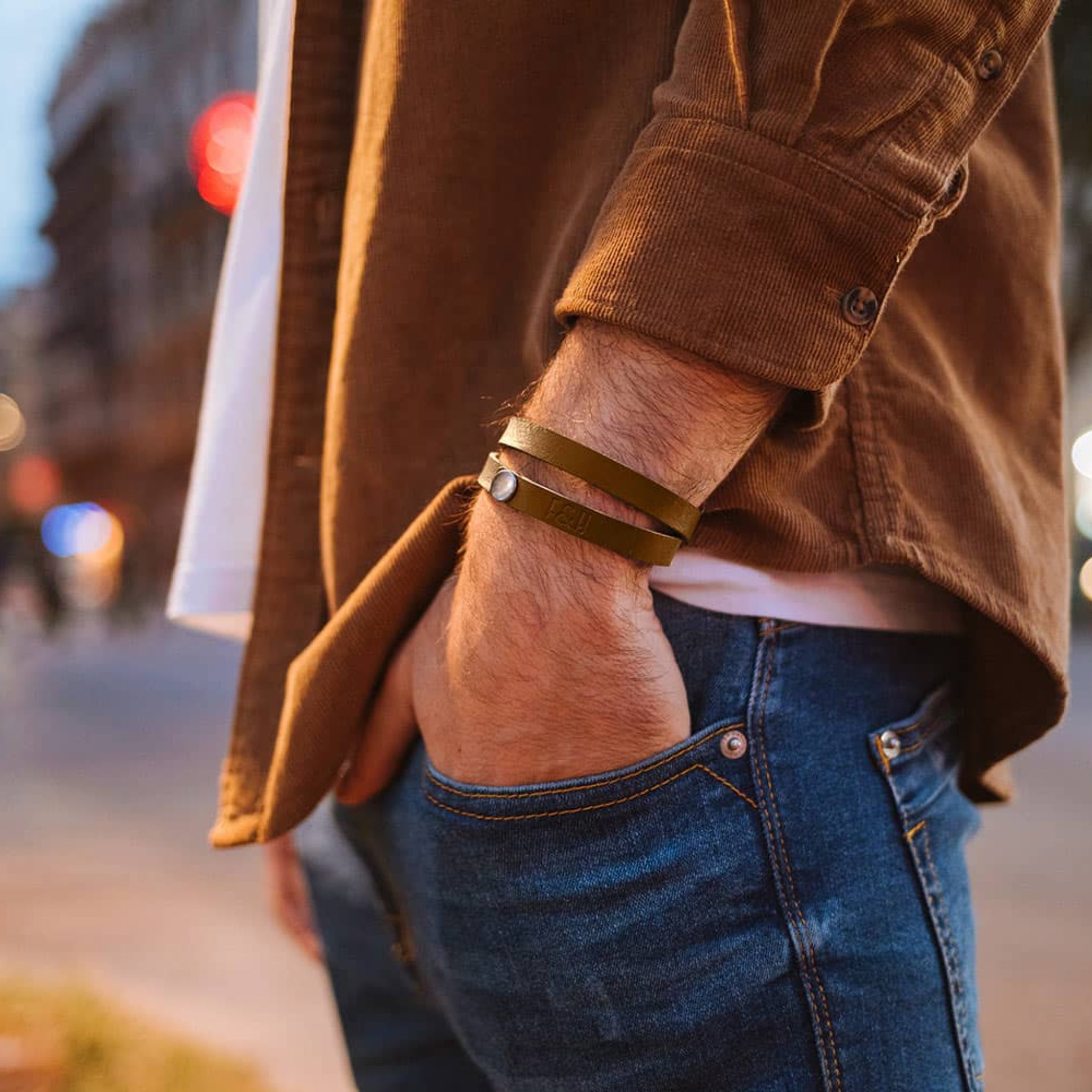 Nahaufnahme eines Mannes in Jeans und braunem Hemd mit einer Hand in der Hosentasche und einem Armband.