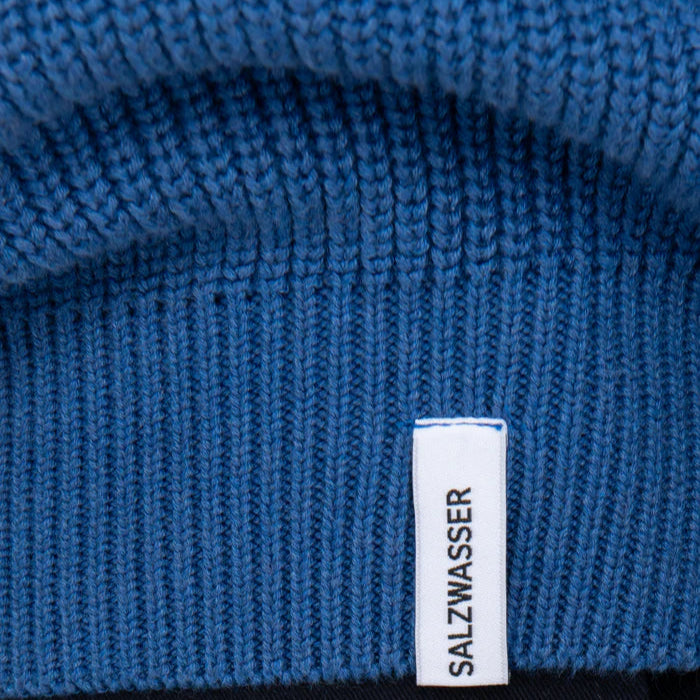 Nahaufnahme eines blauen Gewirkes mit einem aufgenähten weißen Schild, auf dem in schwarzen Großbuchstaben das Wort SALZWASSER steht.