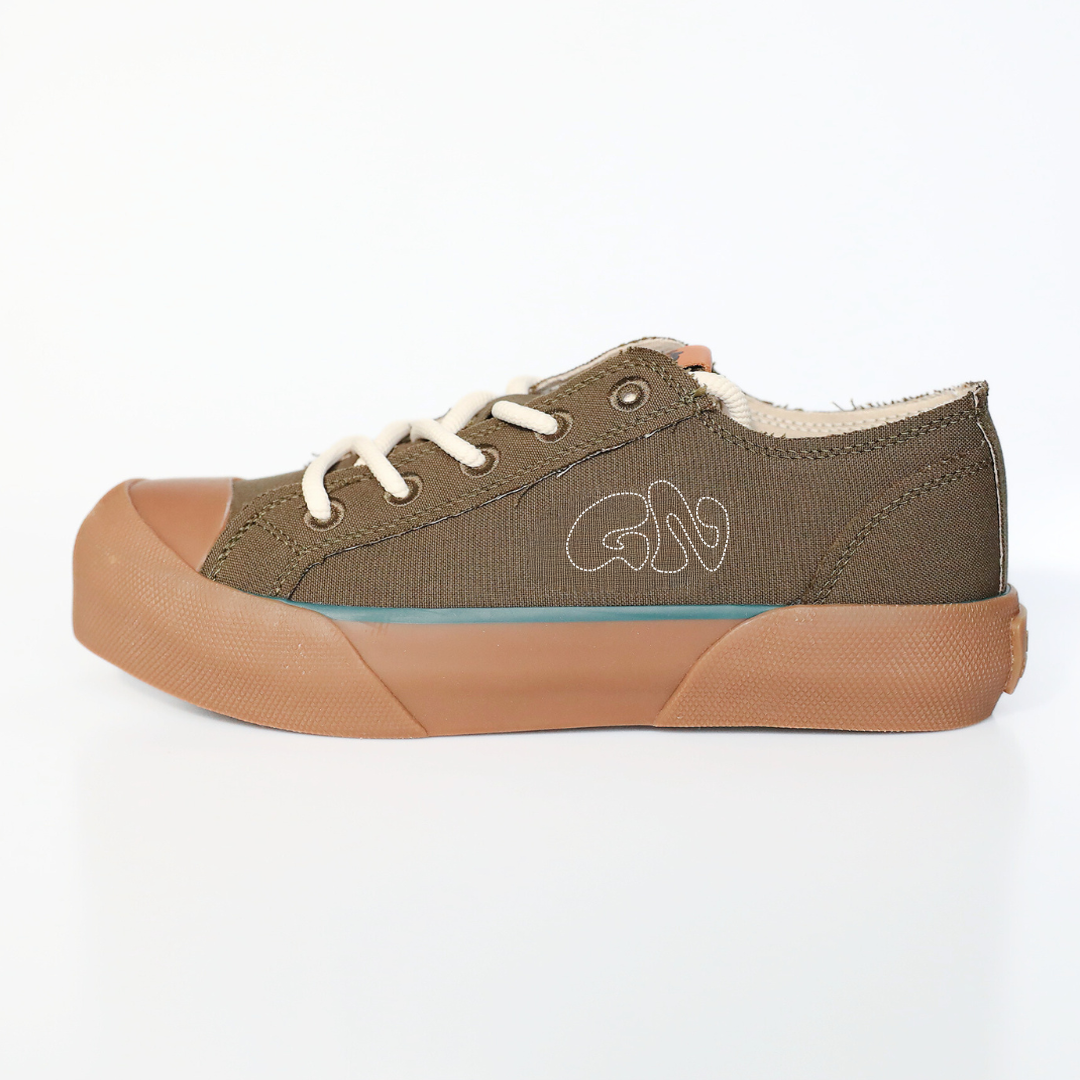 Grüner Sneaker mit cremefarbenen Schnürsenkeln und brauner Gummisohle auf weißem Hintergrund.