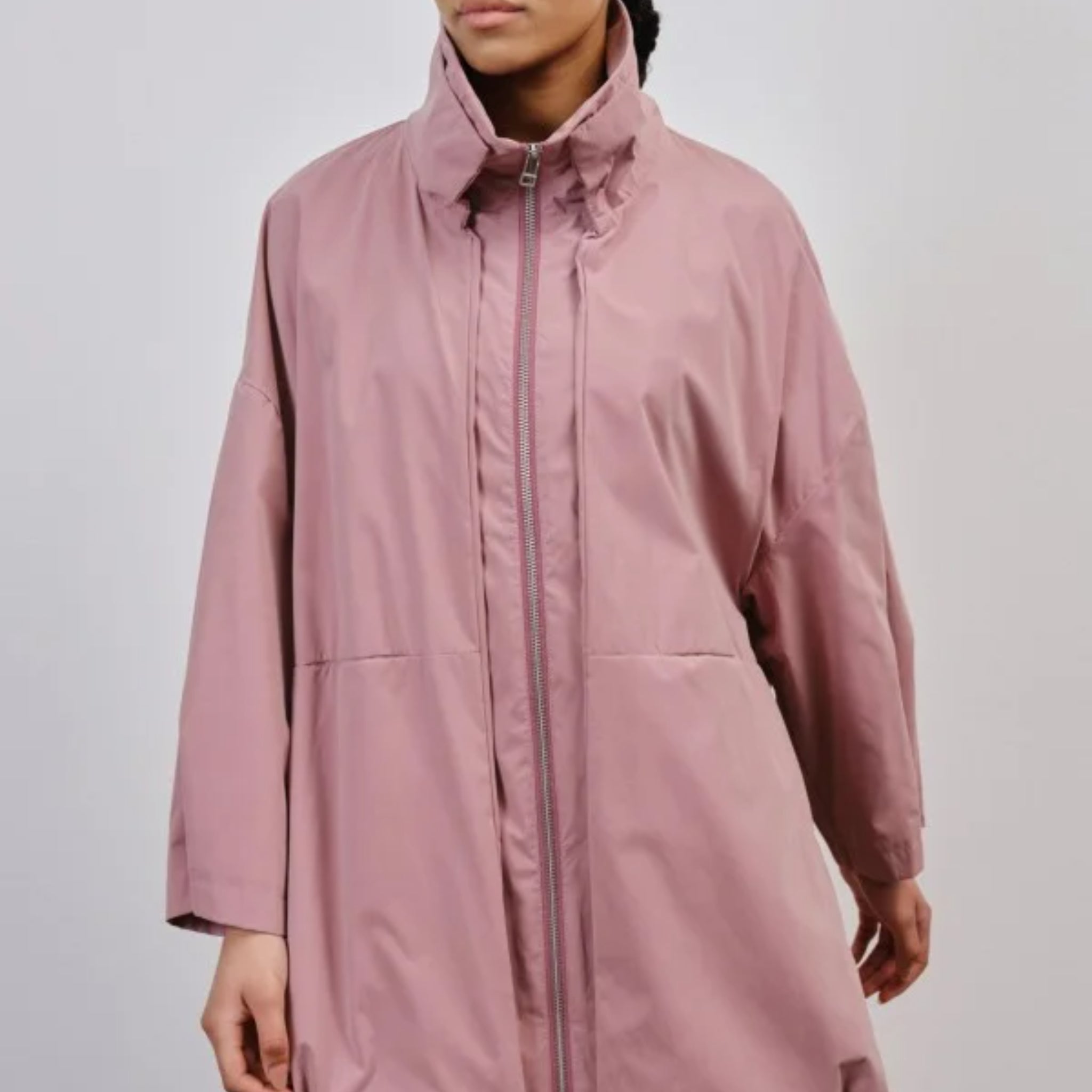 Person trägt einen langen, rosafarbenen Mantel mit hohem Kragen und Reißverschluss, der teilweise geöffnet ist.