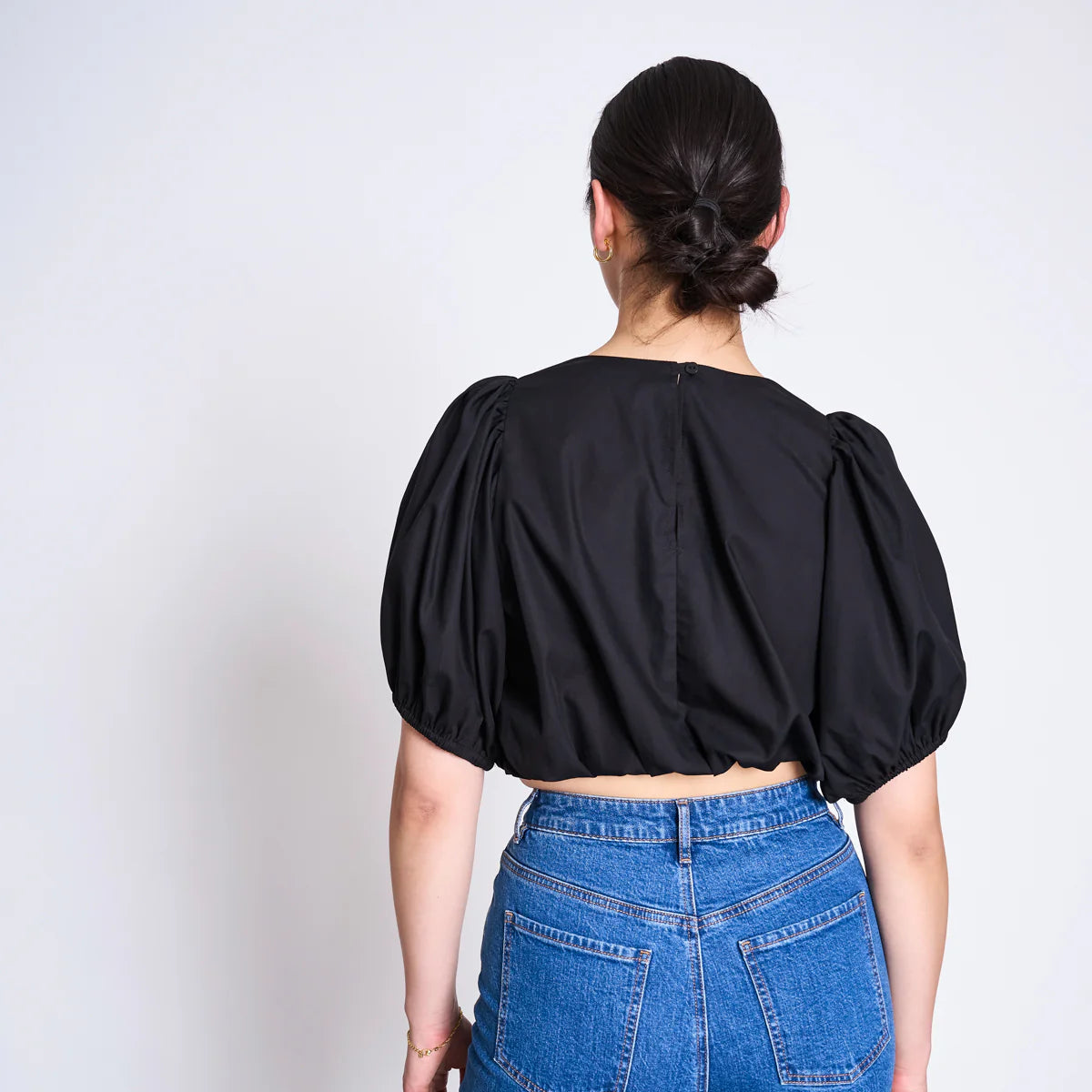Frau von hinten in schwarzem, kurzem Oberteil mit Puffärmeln und blauer Jeans mit Pferdeschwanz-Frisur.