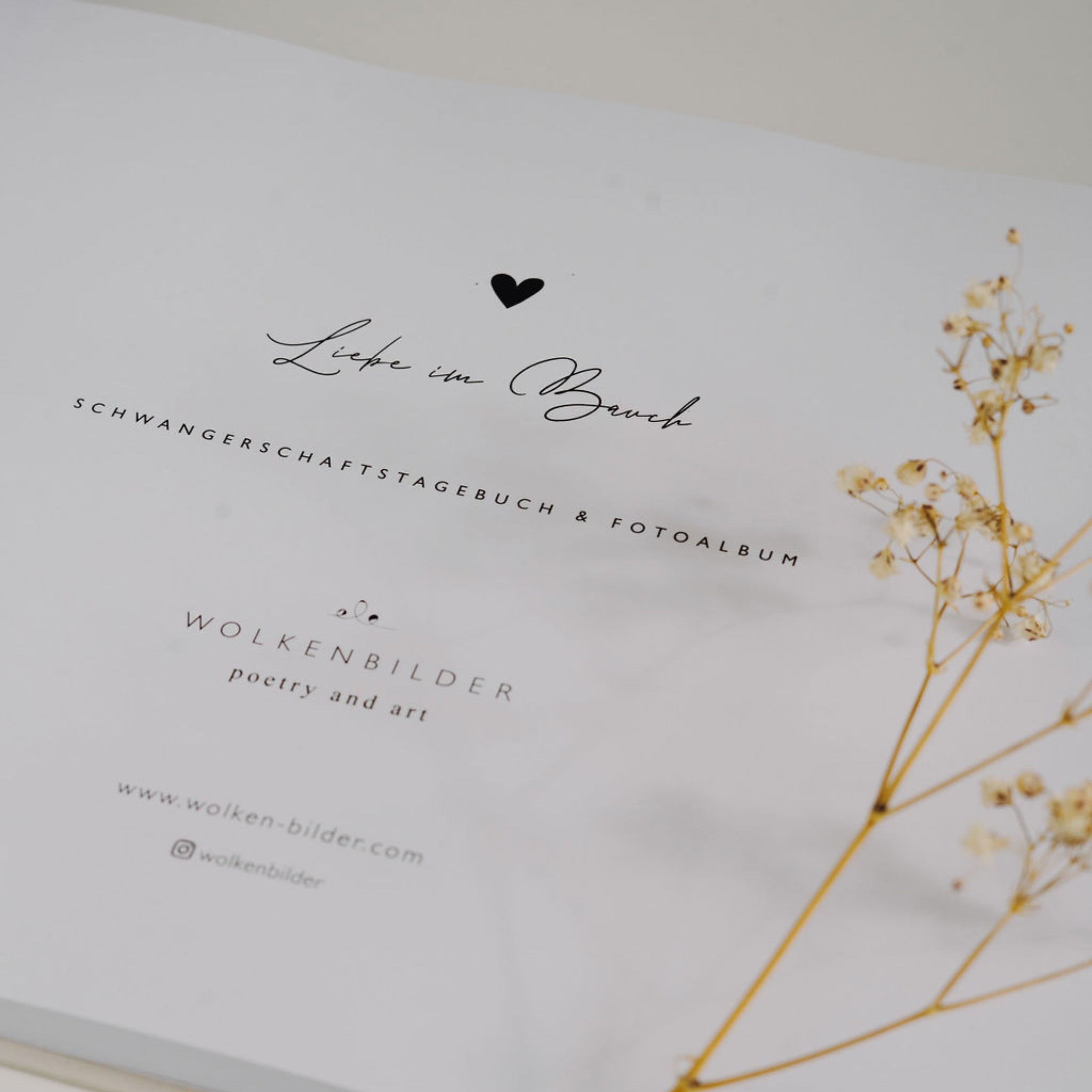 Weiße Buchseite mit der Aufschrift "Liebe im Bauch", begleitet von zarten, getrockneten Blüten.