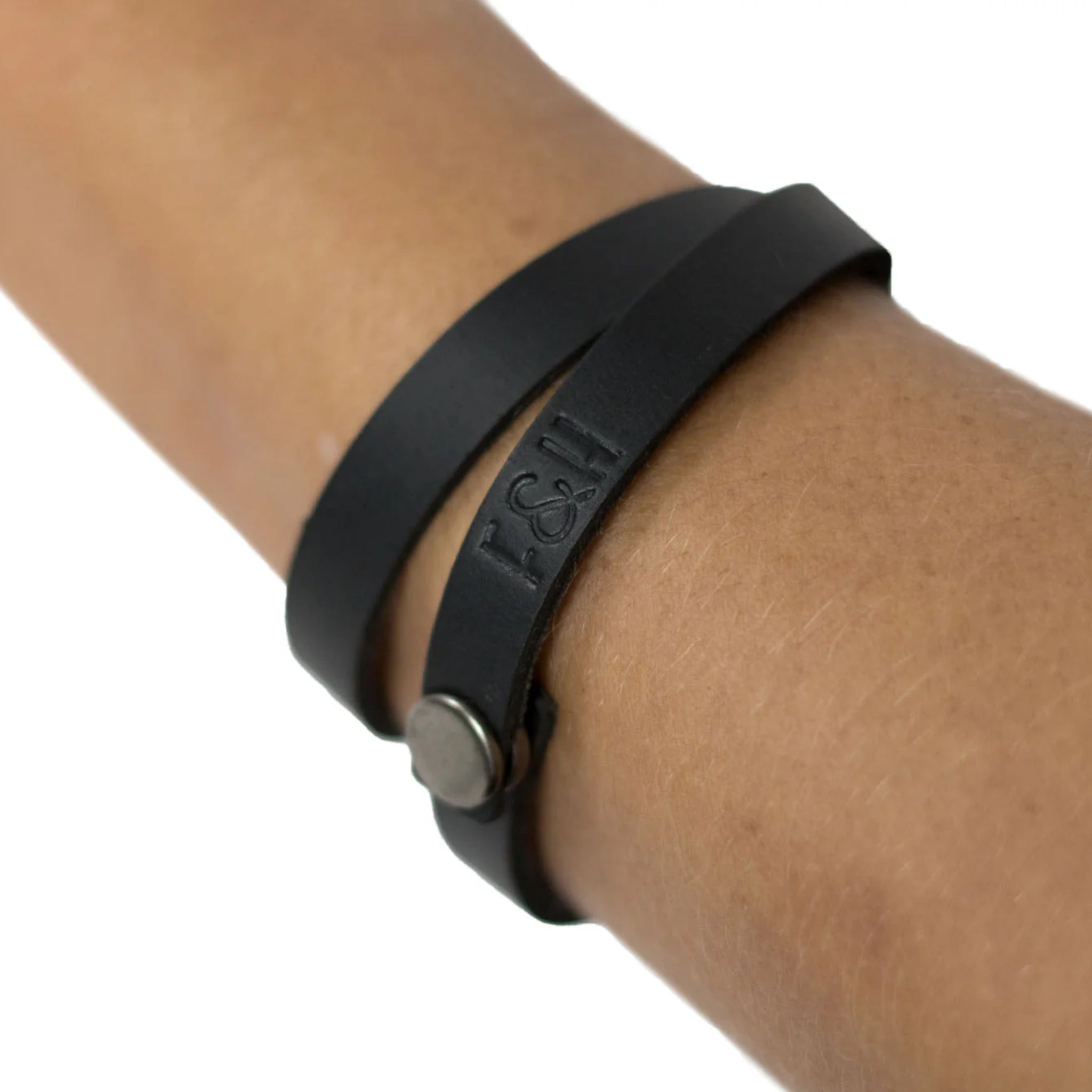 Nahaufnahme eines schwarzen Lederarmbands mit Prägung "F&H", getragen um ein Handgelenk.