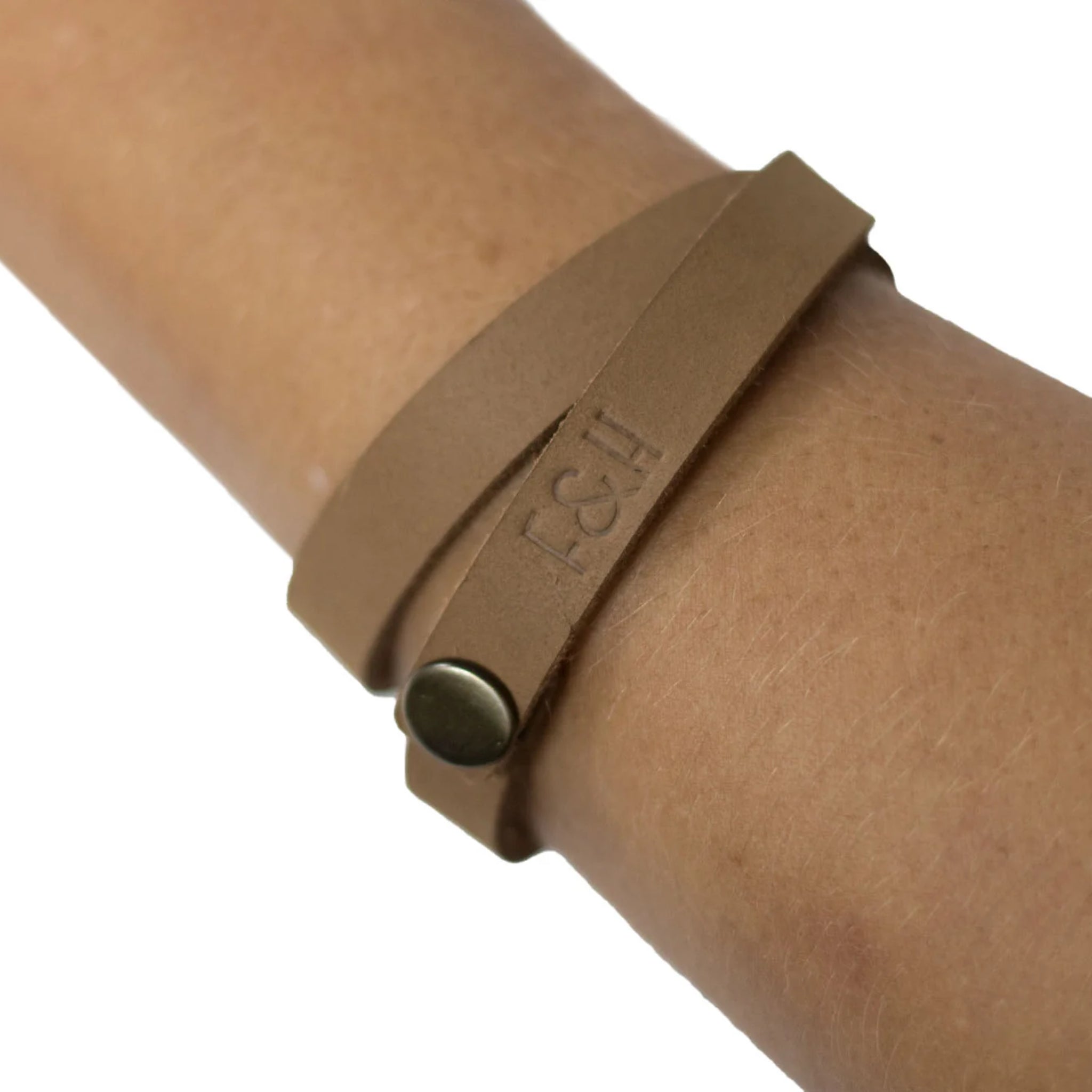 Nahaufnahme eines Handgelenks mit einem hellbraunen Lederarmband und dem geprägten Schriftzug "F&H".