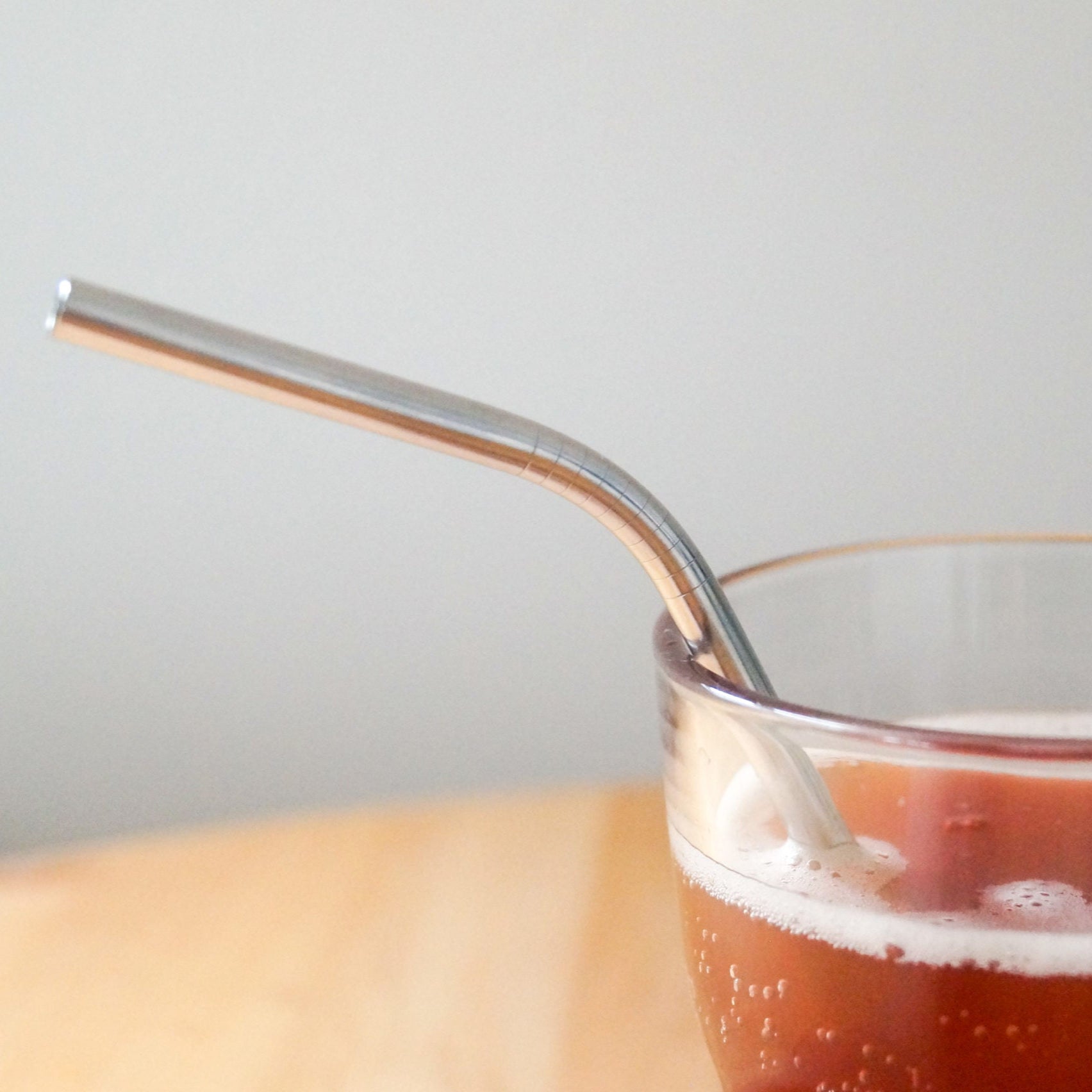 Glas mit rotem Getränk und einem Edelstahlstrohhalm auf einem Holztisch.