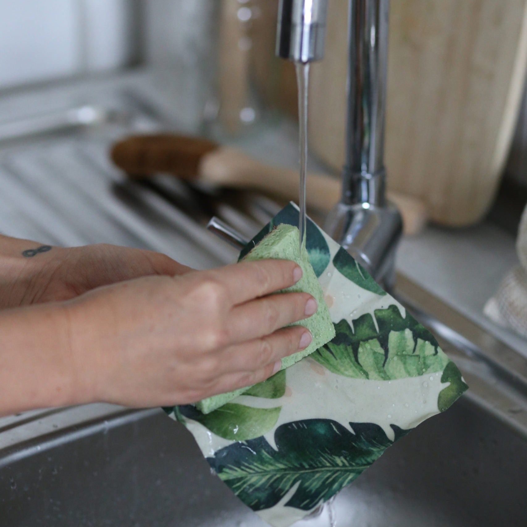 Hände waschen ein buntes Geschirrtuch unter fließendem Wasser in der Spüle.