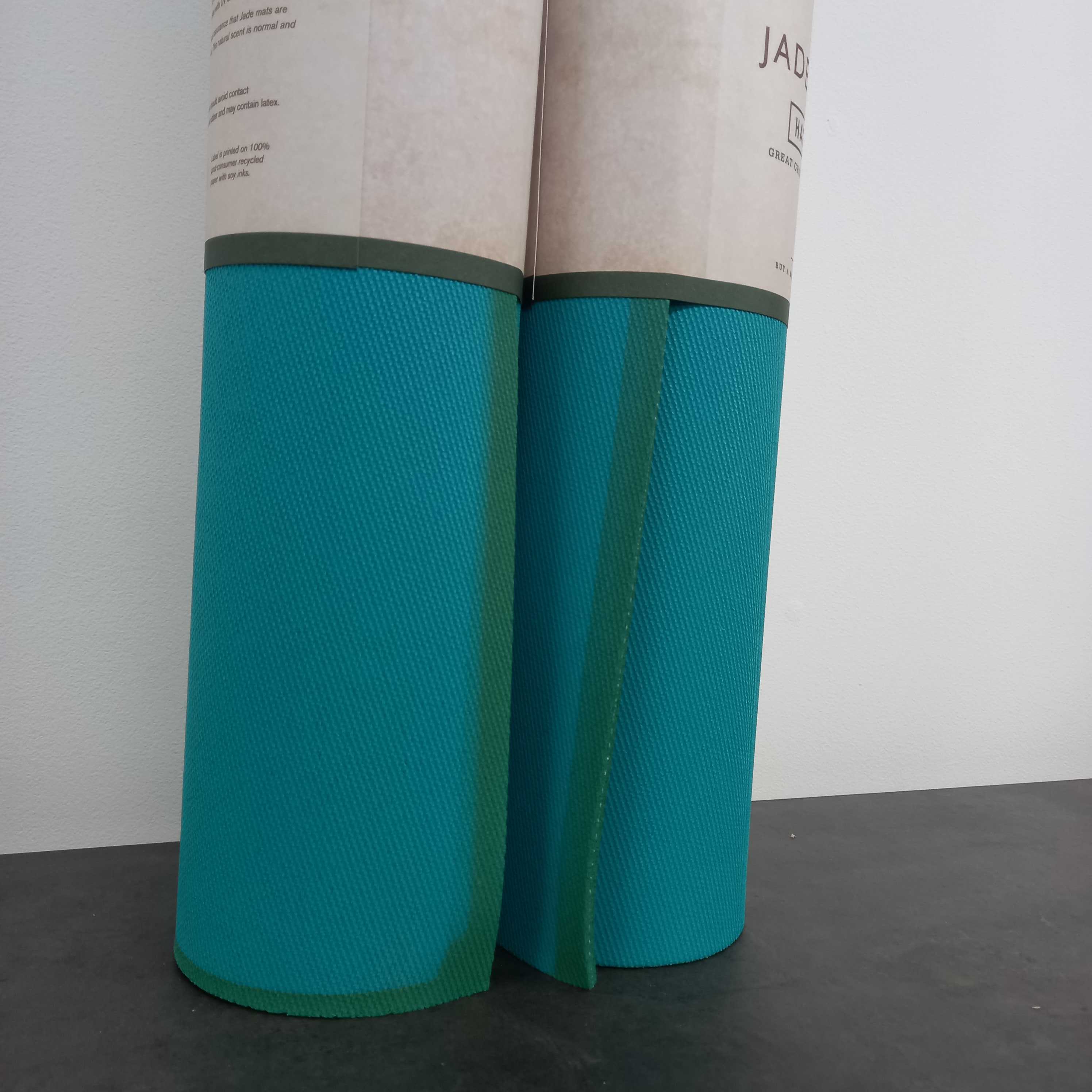 Zwei zusammengerollte blaue Yogamatten stehen aufrecht auf einem dunklen Tisch vor einer weißen Wand.