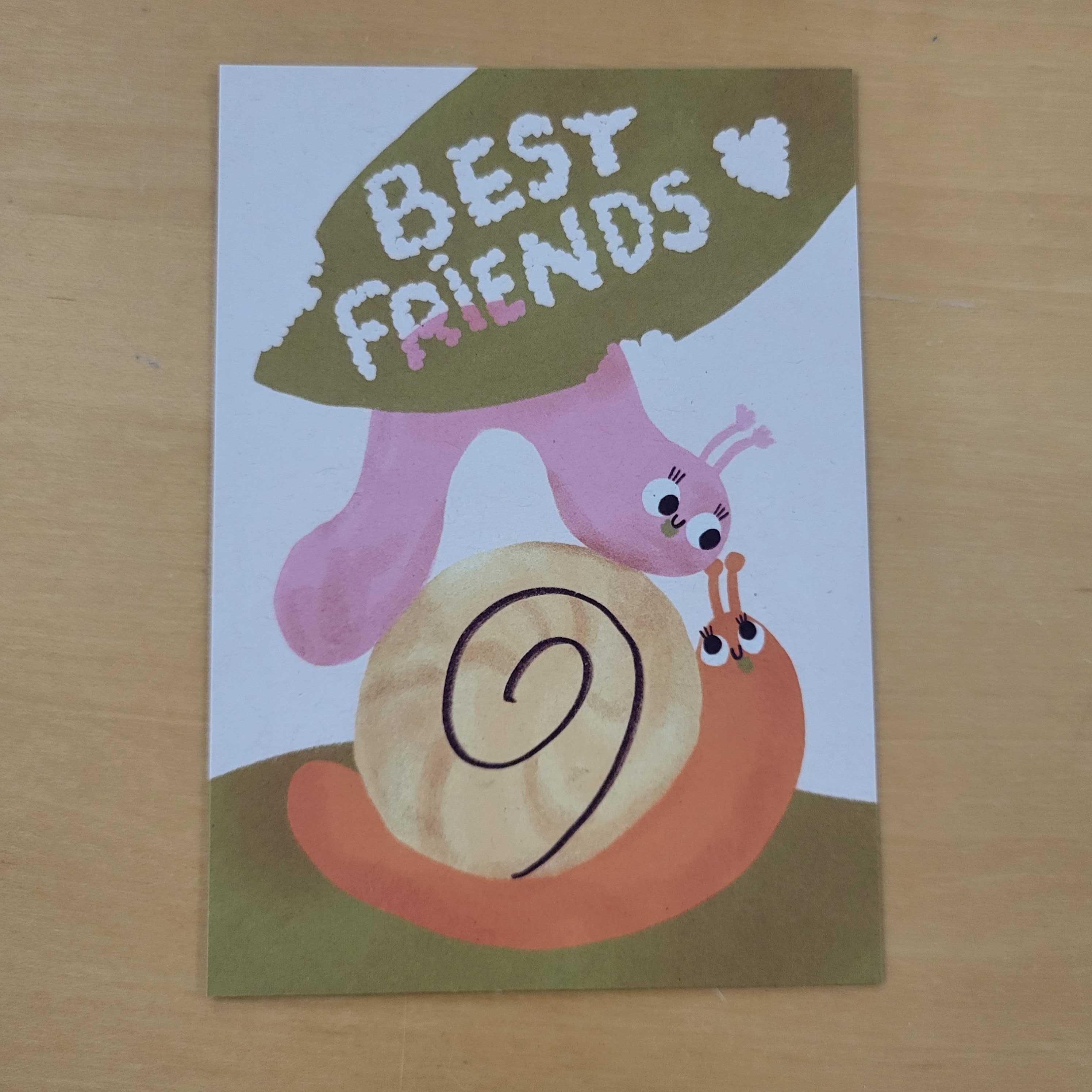 Gemalte Schnecken mit einem Blatt mit der Aufschrift "Best Friends" auf einem Holztisch.