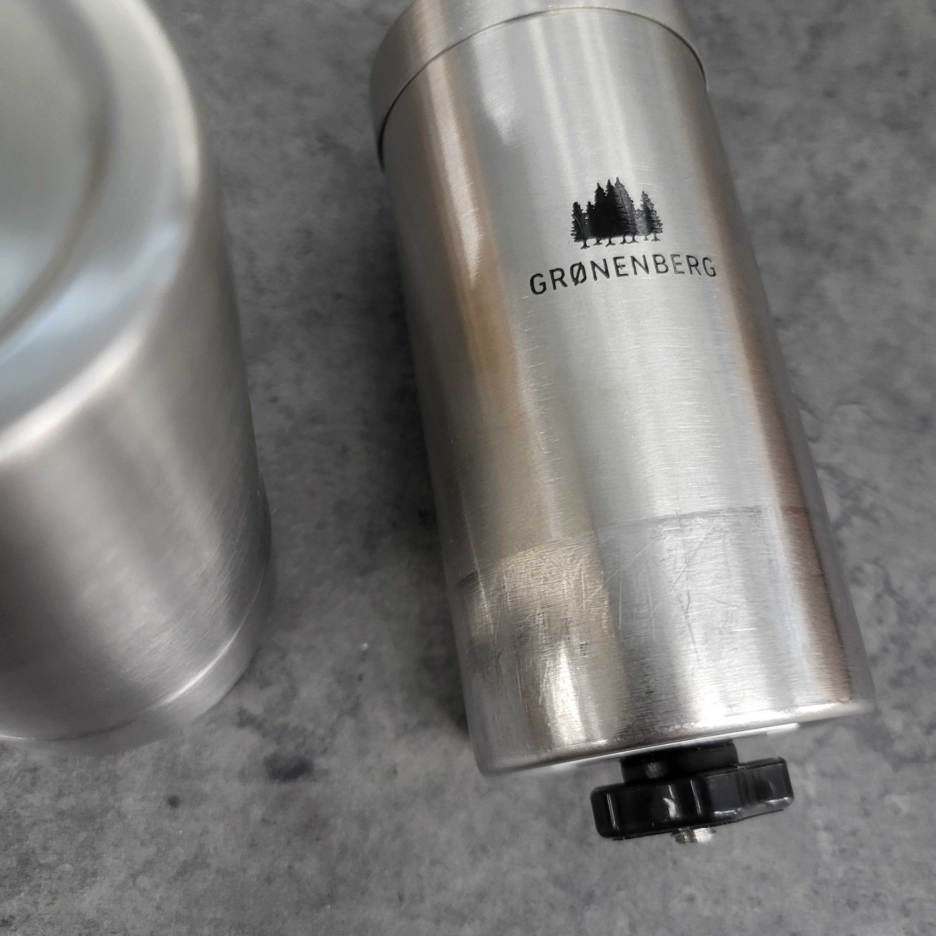 Nahaufnahme einer Metall-Kaffeemühle mit dem Logo „GRØNENBERG“ und einem schwarzen Drehknopf.