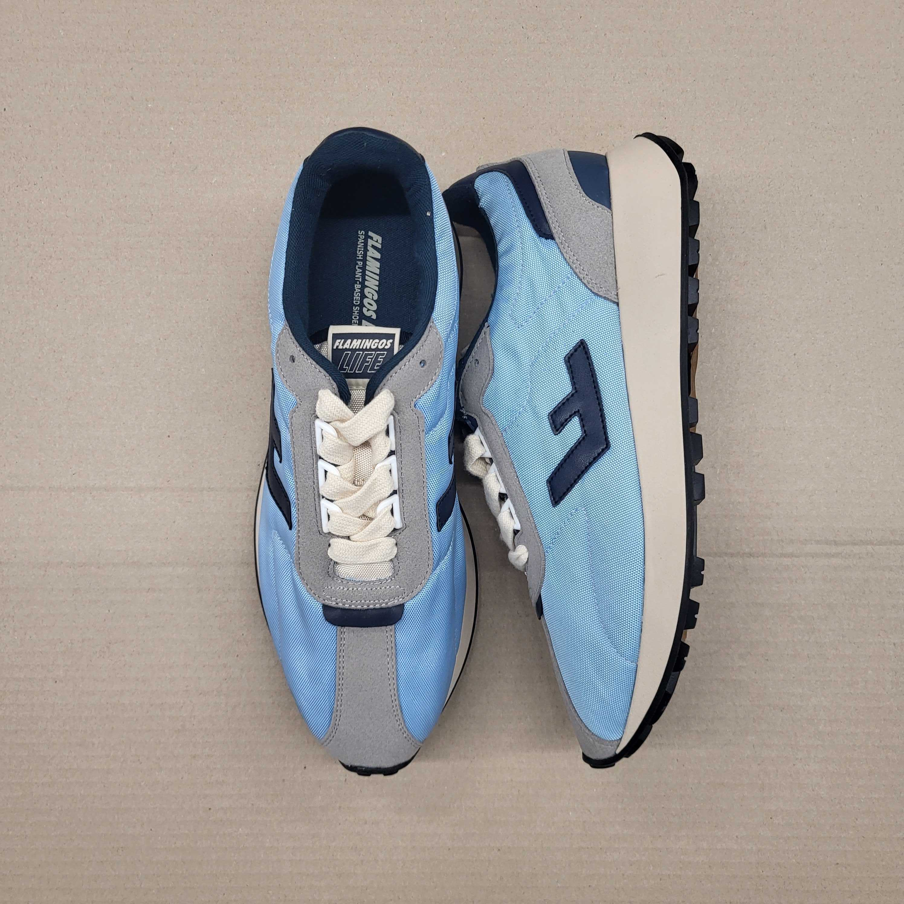 Ein Paar hellblaue Turnschuhe mit grauen und dunkelblauen Akzenten auf einem beigen Hintergrund.