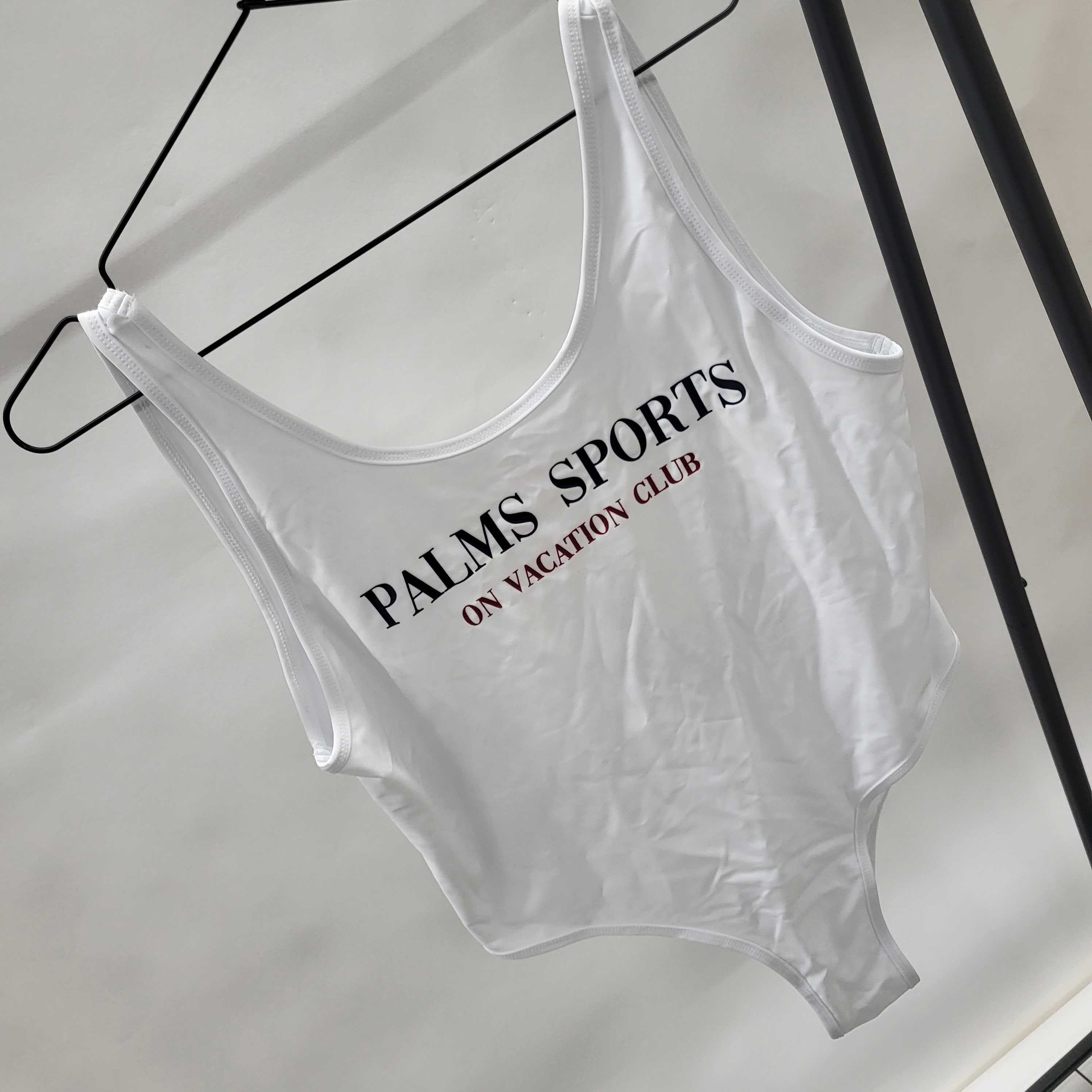 Ein weißer Einteiler mit der Aufschrift "Palms Sports On Vacation Club" hängt an einem schwarzen Kleiderbügel.