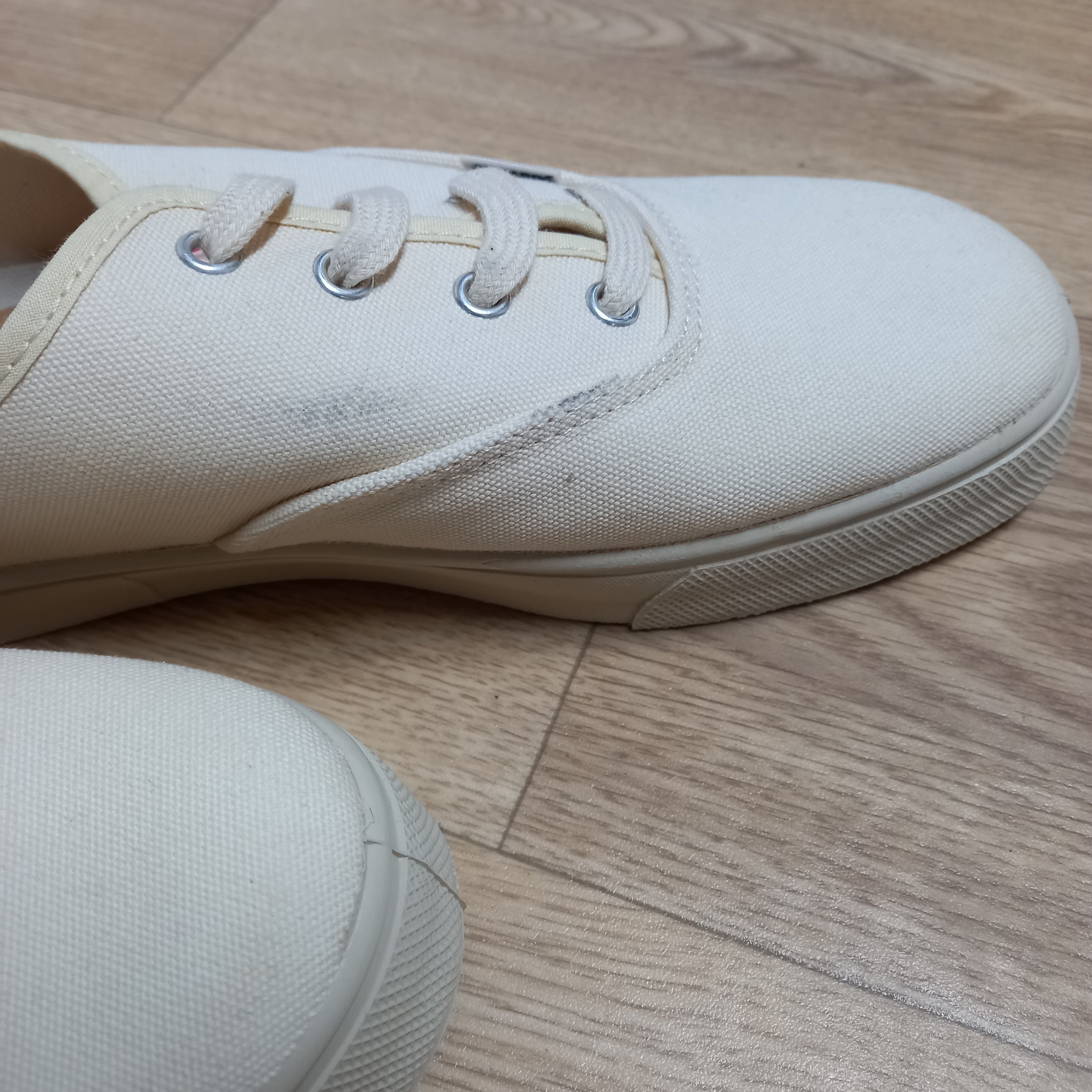 Weiße Leinenschuhe mit breiten Sohlen auf einem Holzboden.