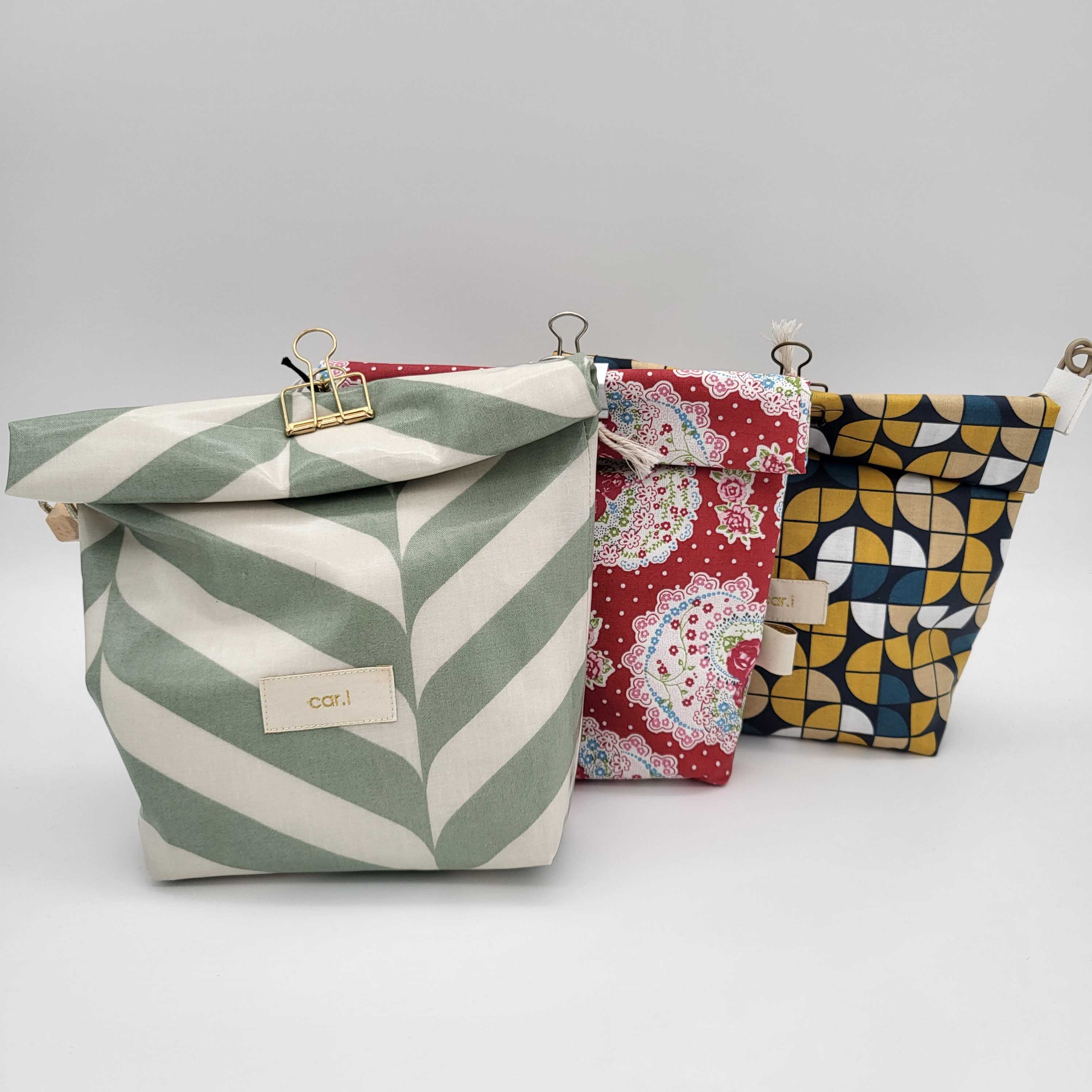 Drei bunte Taschen mit verschiedenen Mustern: grüne Blätter, rote Blumenmuster und geometrische Formen.