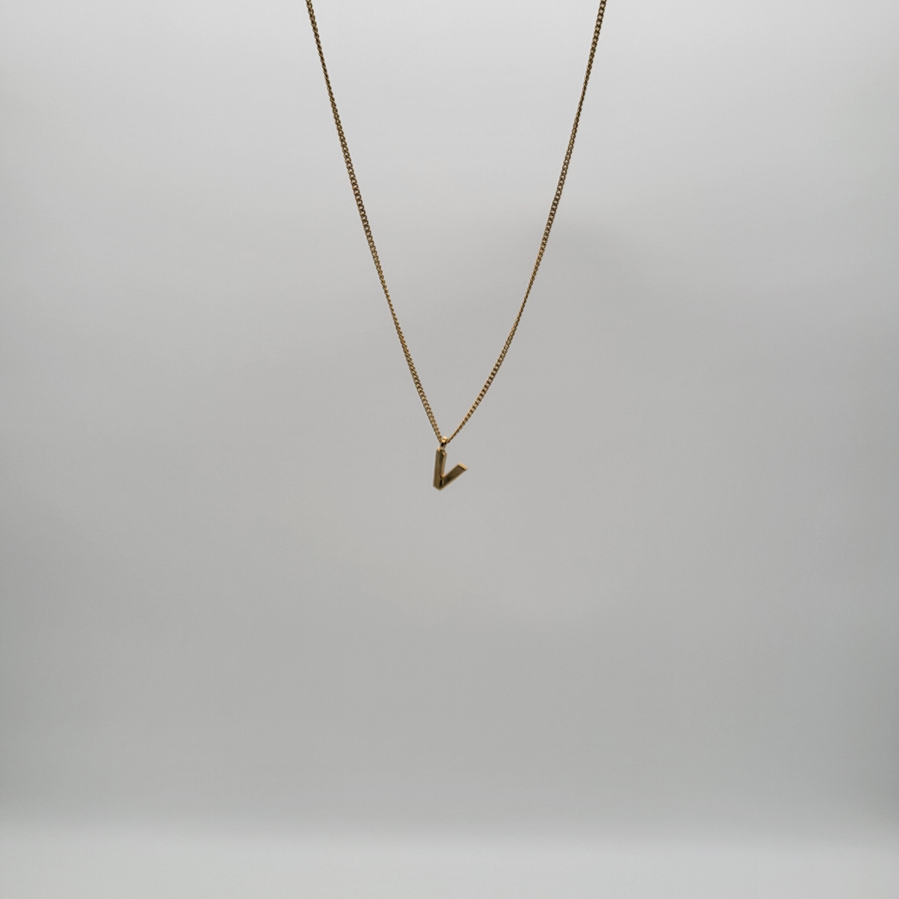Eine einfache Goldkette mit einem kleinen, eckigen Anhänger hängt vor einem schlichten, hellgrauen Hintergrund.