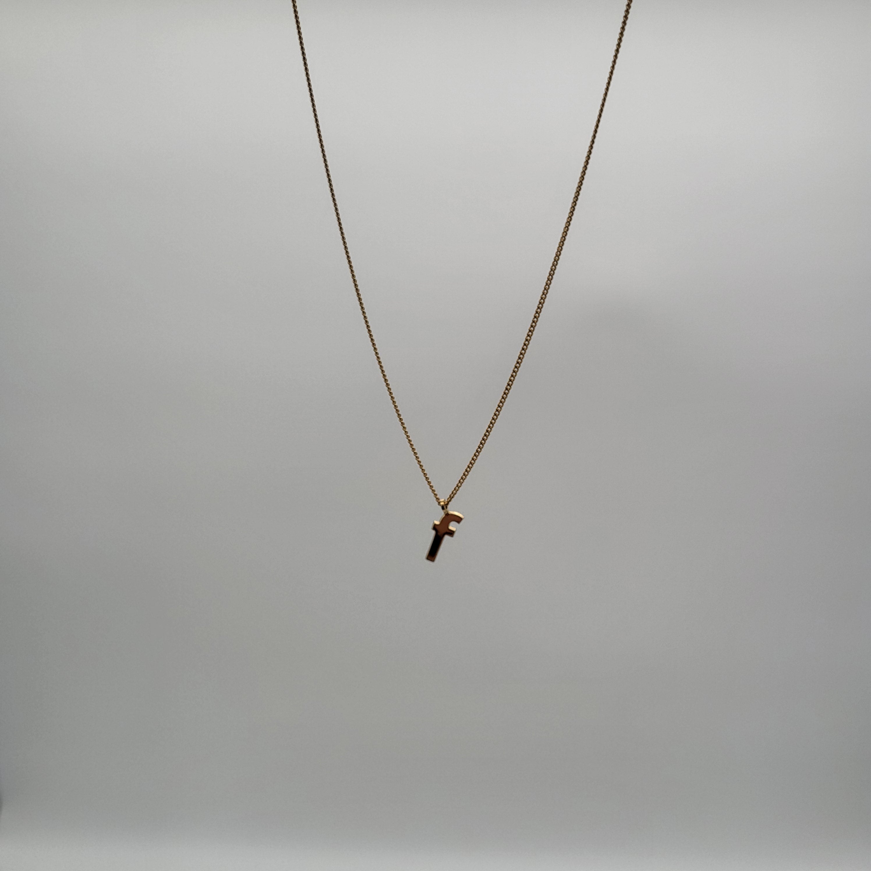 Eine goldene Halskette mit einem kleinen Kreuzanhänger, der an einer dünnen Kette hängt, steht in der Mitte vor einem schlichten, hellgrauen Hintergrund.