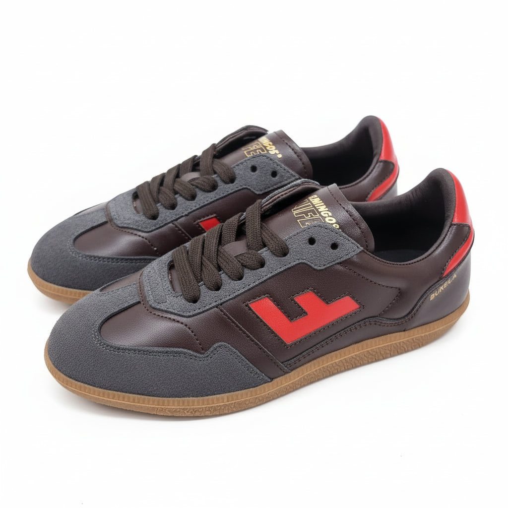 Ein Paar braun-graue Turnschuhe mit roten Akzenten, darunter ein großes rotes F an der Seite und eine rote Fersenlasche. Die Schuhe haben Gummisohlen und schwarze Schnürsenkel und stehen auf einem hellen Boden.